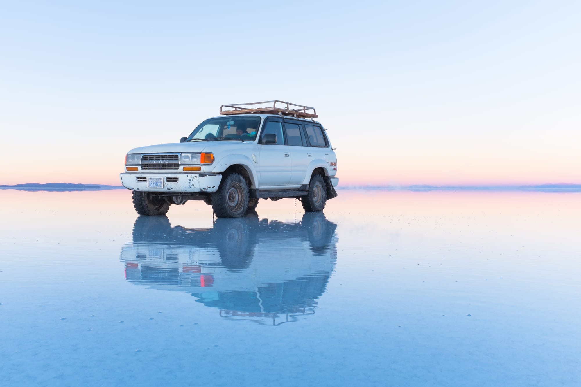 A person standing on a thin sheet of water over a white salt flat that perfectly mirrors the clouded sky