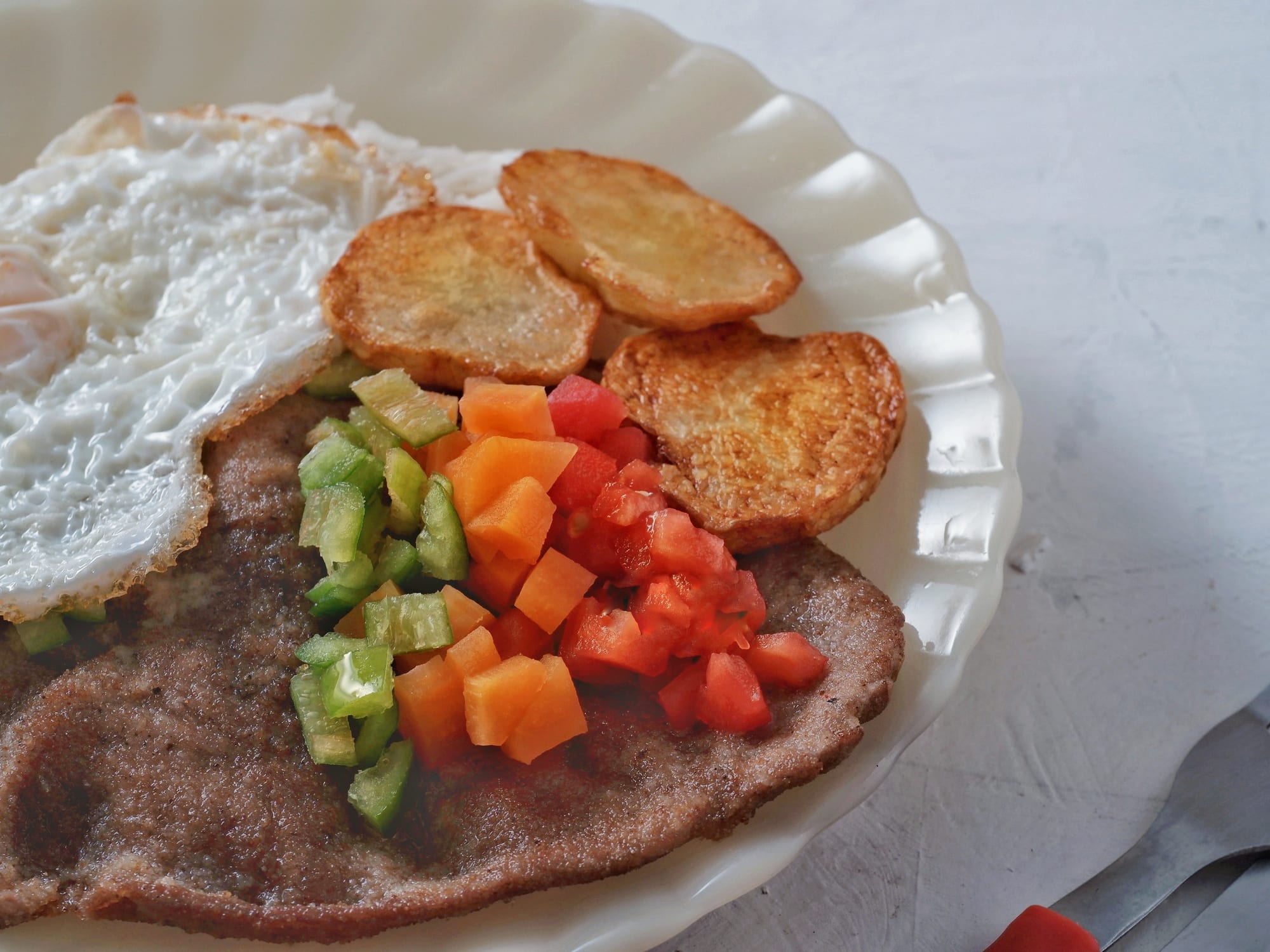 A plate with rice, a thin breaded beef cutlet, fries, salad and a fried egg on top