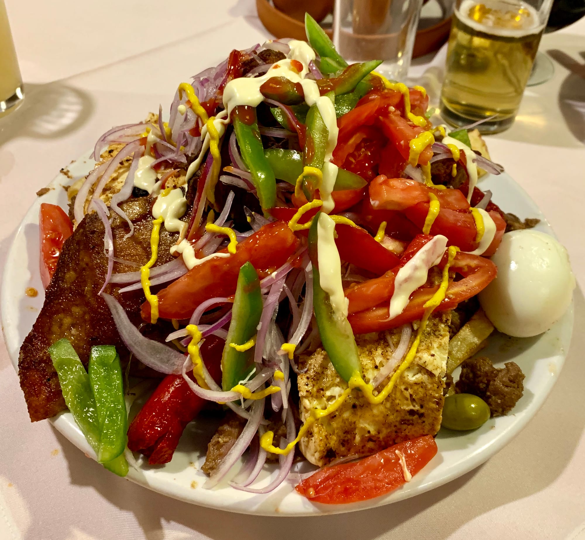 A large plate piled with fried beef, sausage, fries, onion, pepper and a fried egg