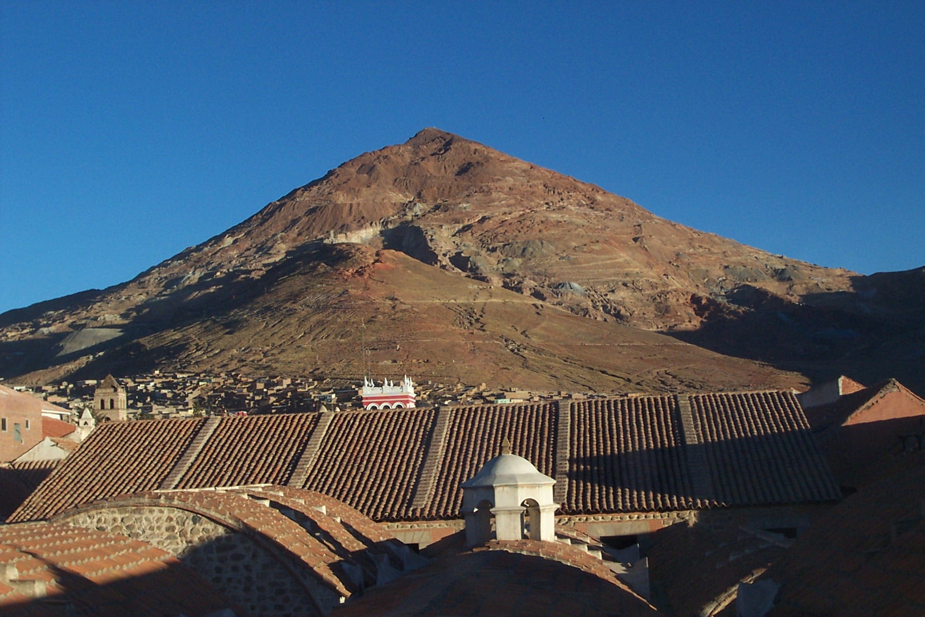 A conical reddish mountain rising behind the rooftops and church towers of a colonial city