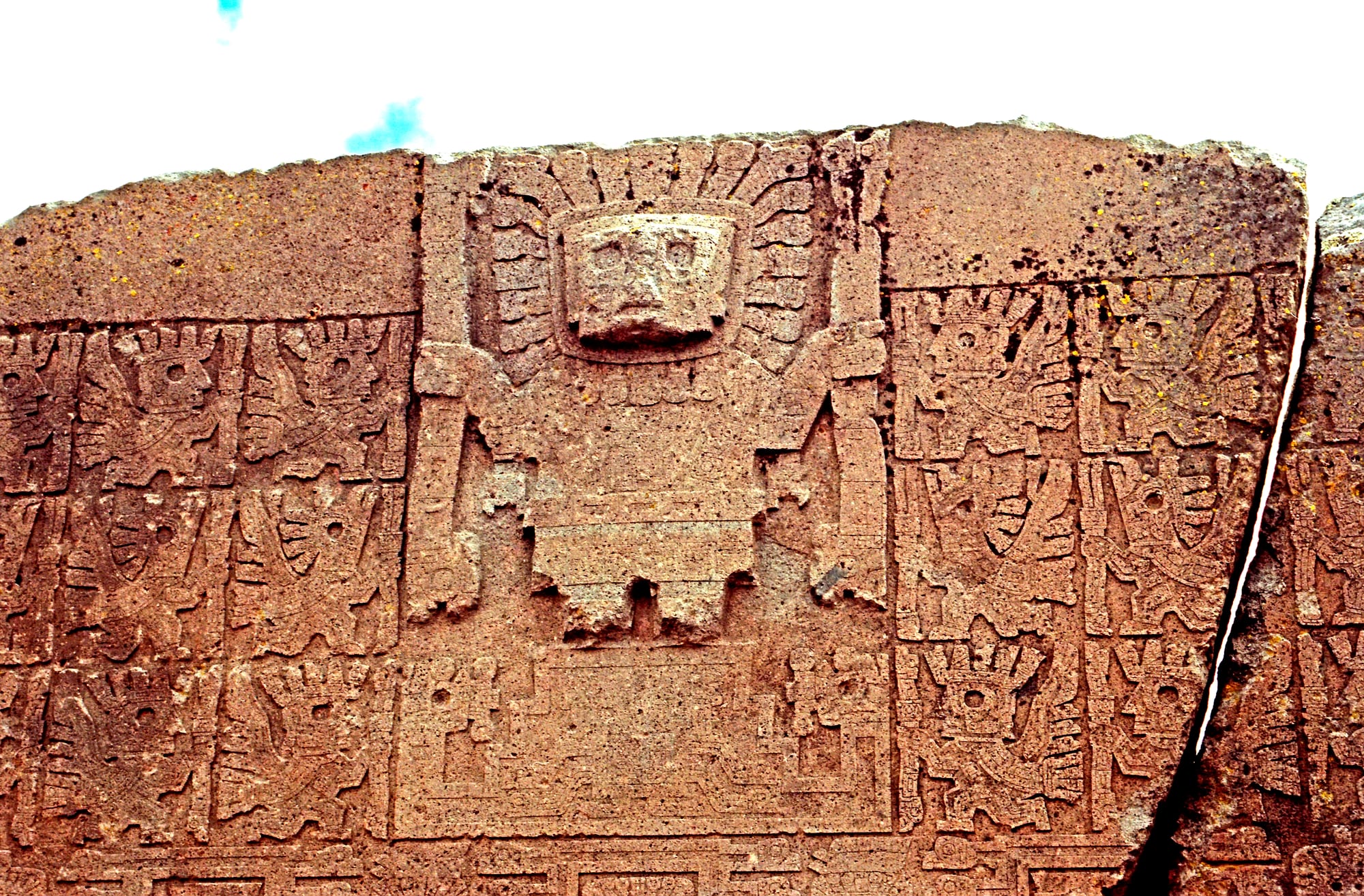 A monolithic stone gateway carved with a central figure and rows of winged attendants, on a bare high plain