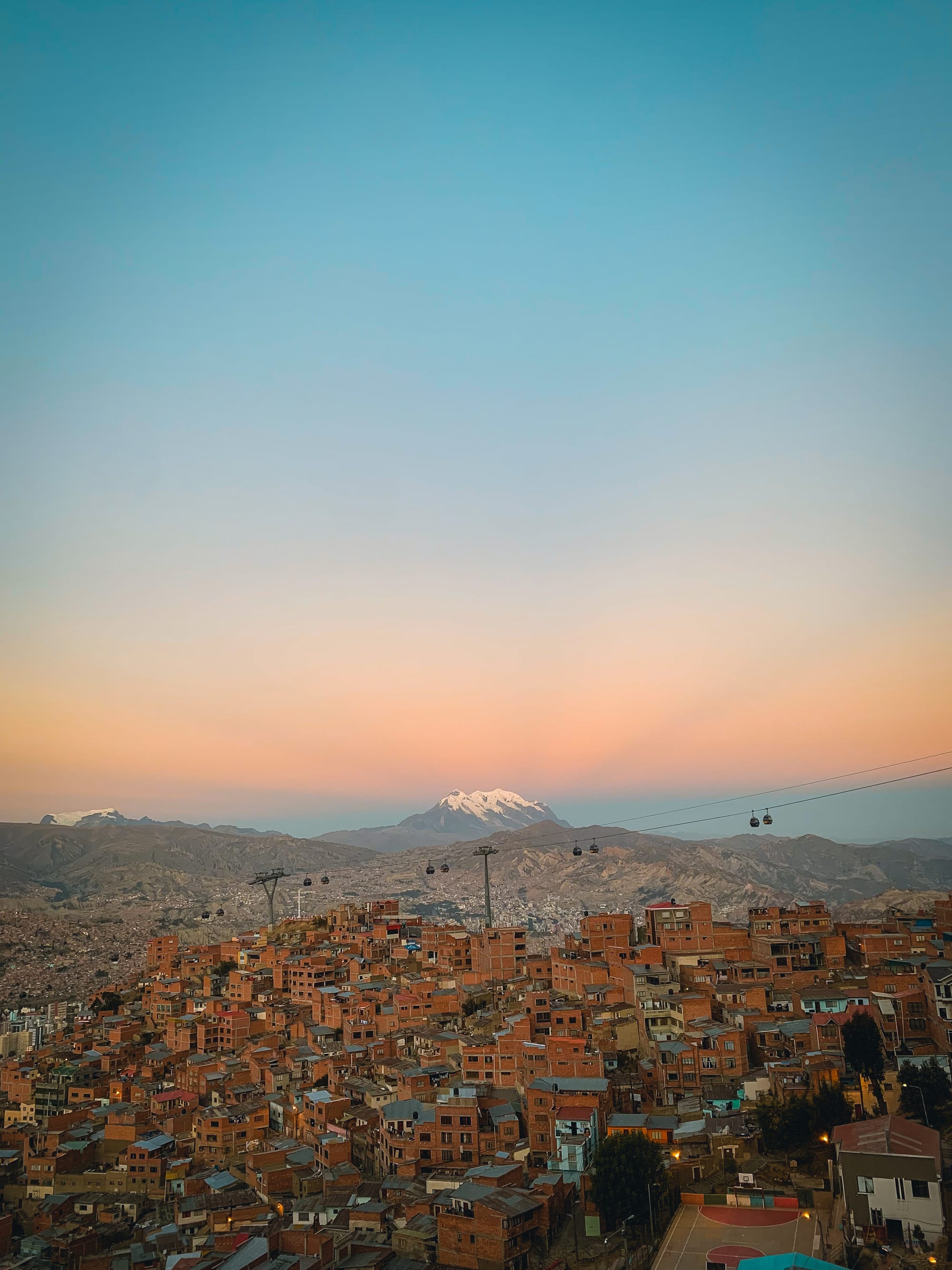 A dense city filling a deep bowl in the mountains, packed up the slopes below a huge snow peak