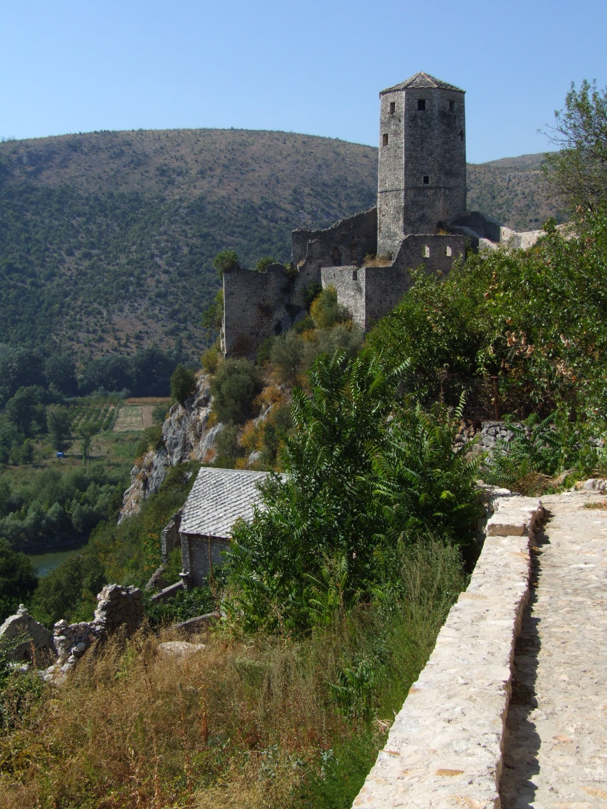 A stone Ottoman town climbing a steep hillside to a round fort tower, river below