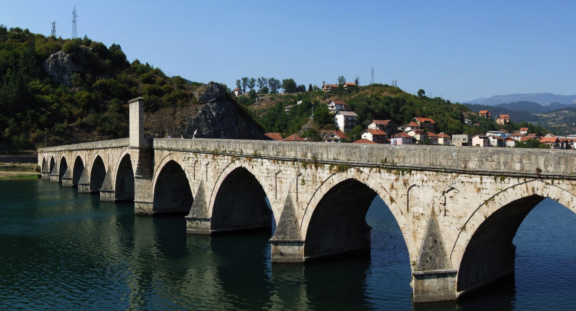 A long, low, many-arched Ottoman stone bridge across a wide green river