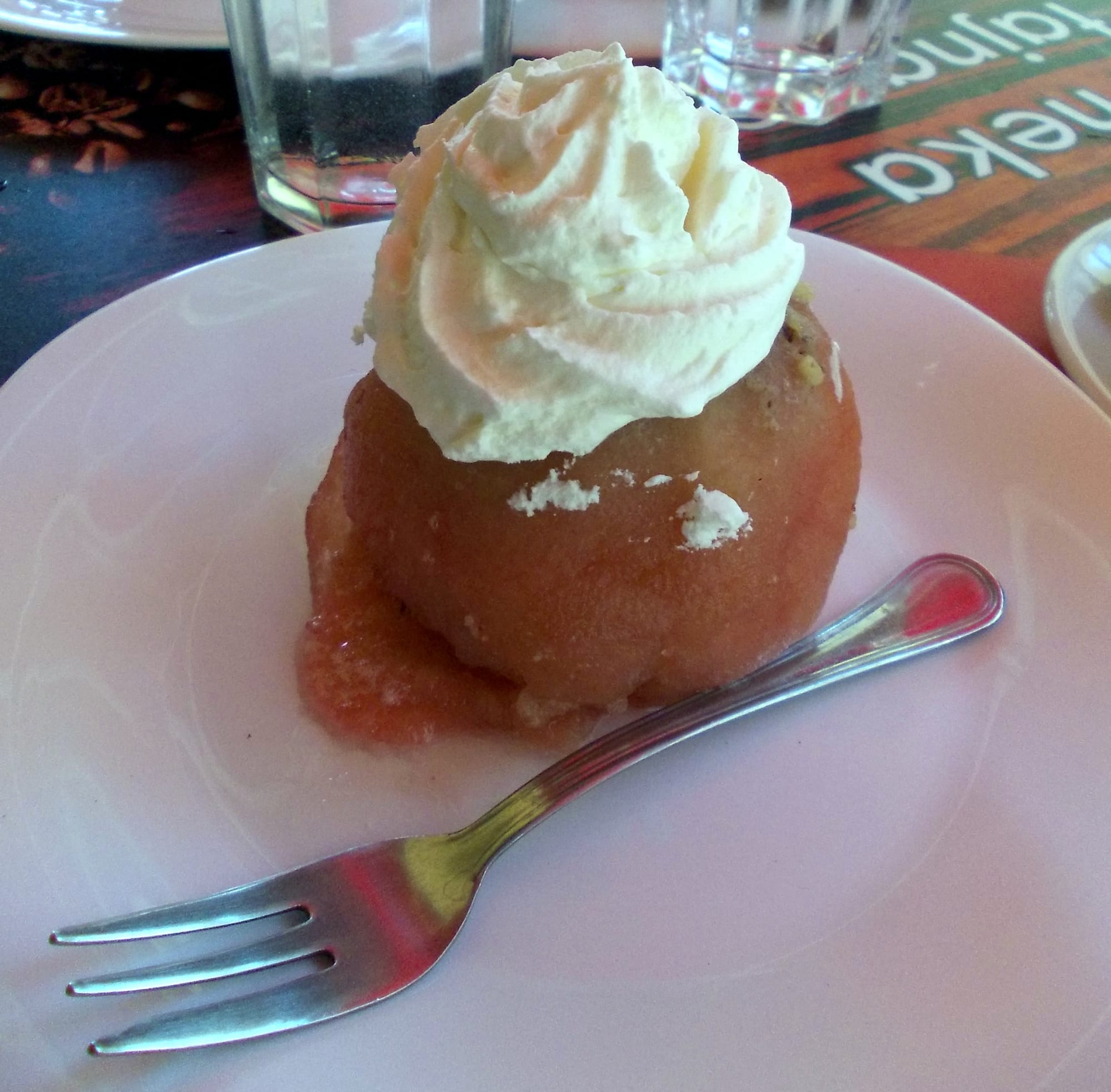 A whole poached apple filled with a pale walnut mixture and topped with whipped cream, on a plate