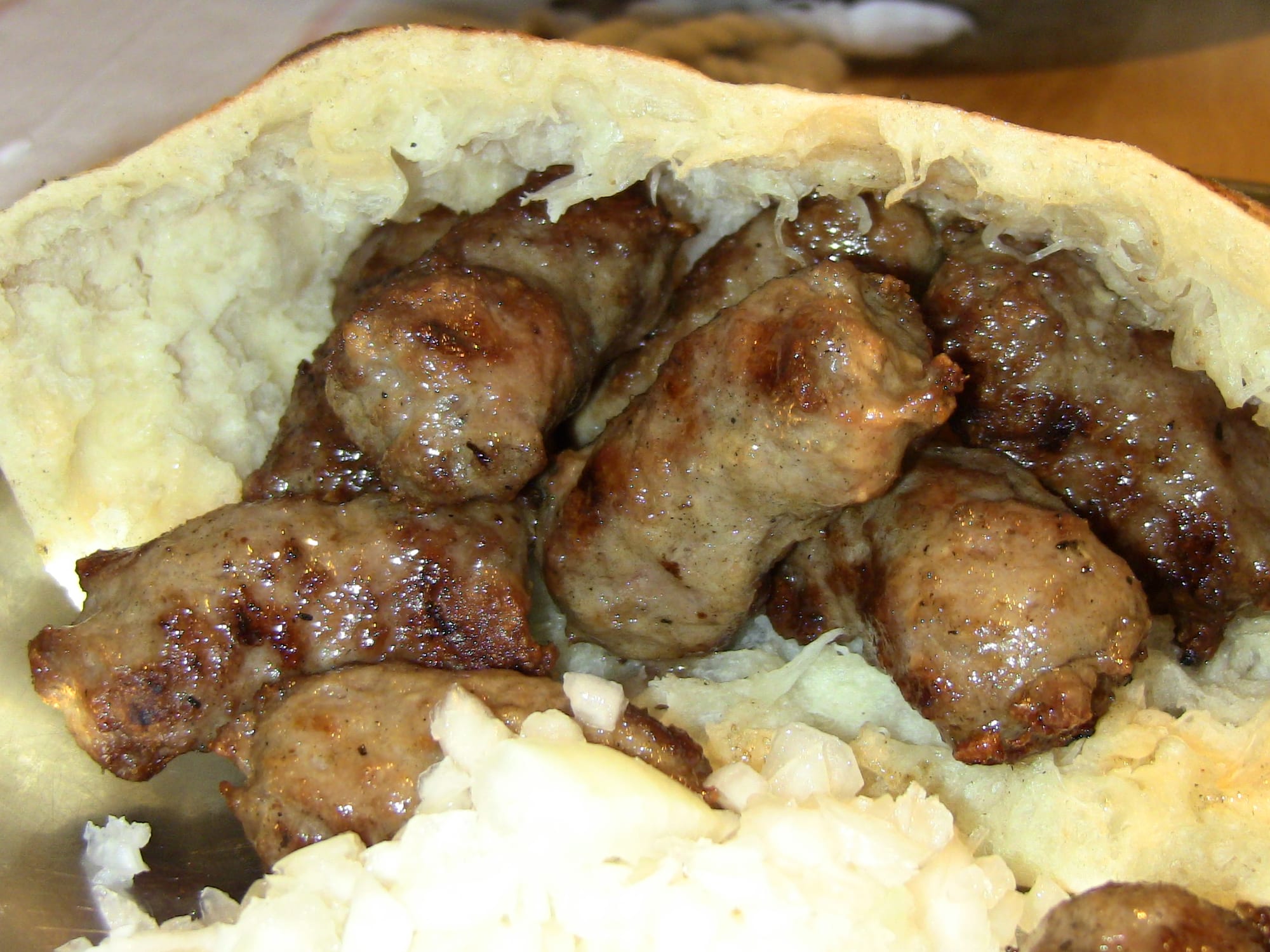 A plate of small grilled minced-meat fingers arranged on a piece of flatbread with chopped raw onion