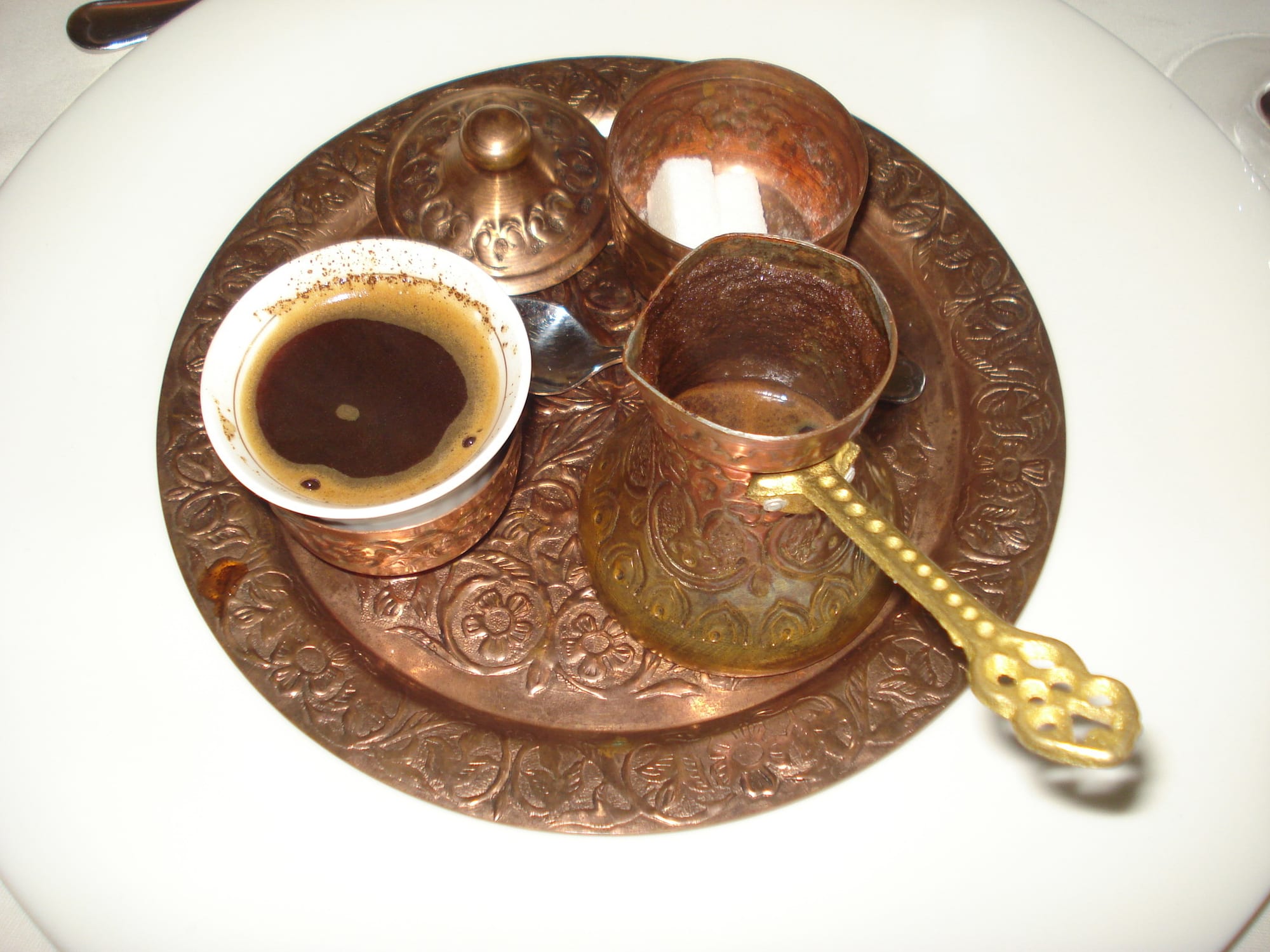 A small copper coffee pot beside a cup of dark coffee and a sugar bowl