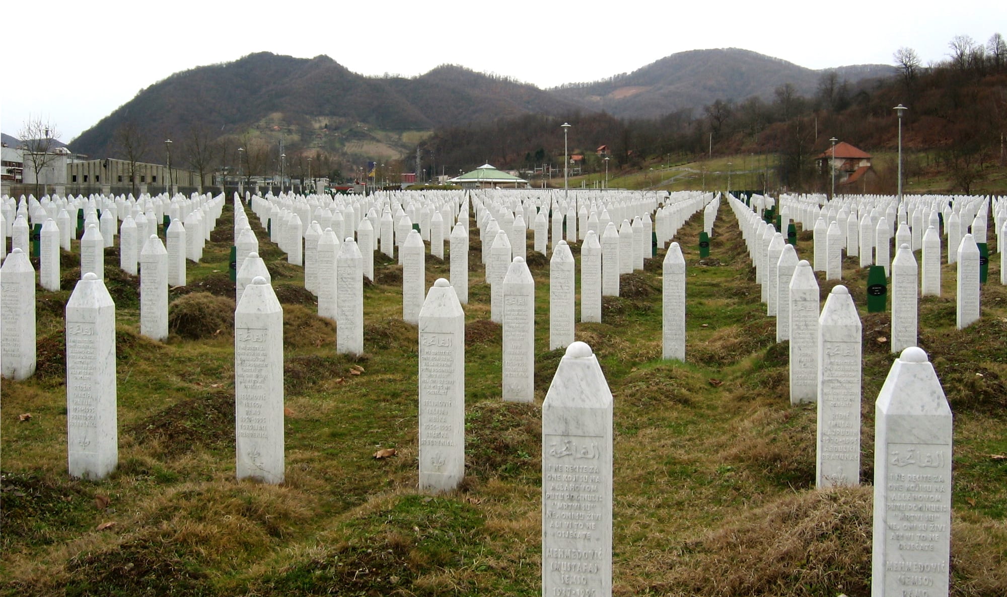 Rows of identical white obelisk gravestones covering a green hillside cemetery