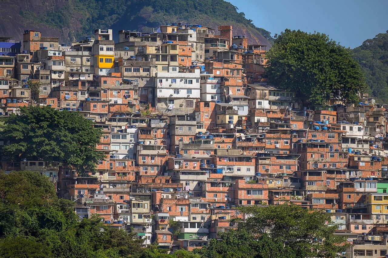 A dense hillside of small, self-built brick and concrete houses stacked closely together, with water tanks on many rooftops