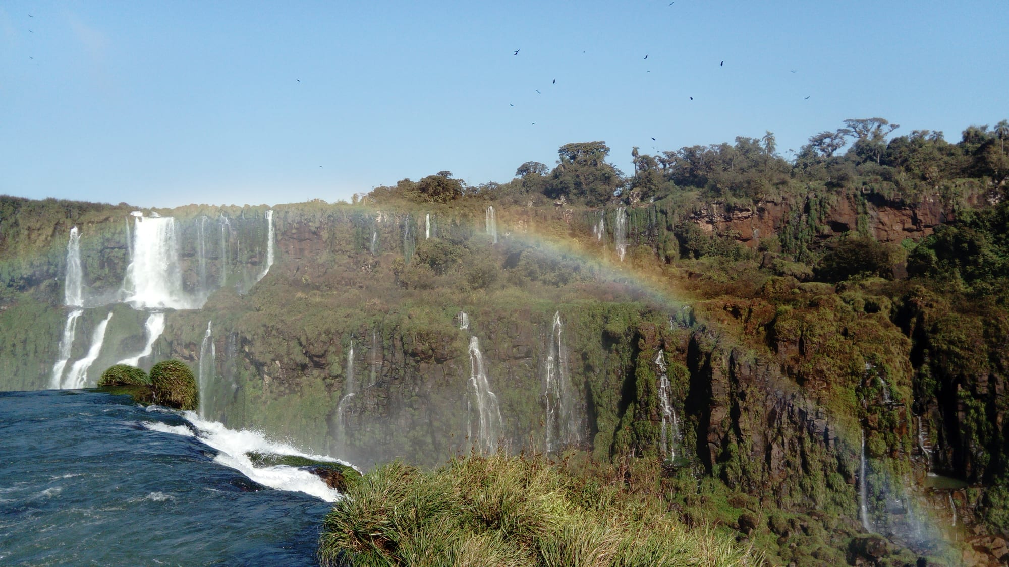 A vast curved wall of waterfalls tumbling through jungle, rainbows in the spray