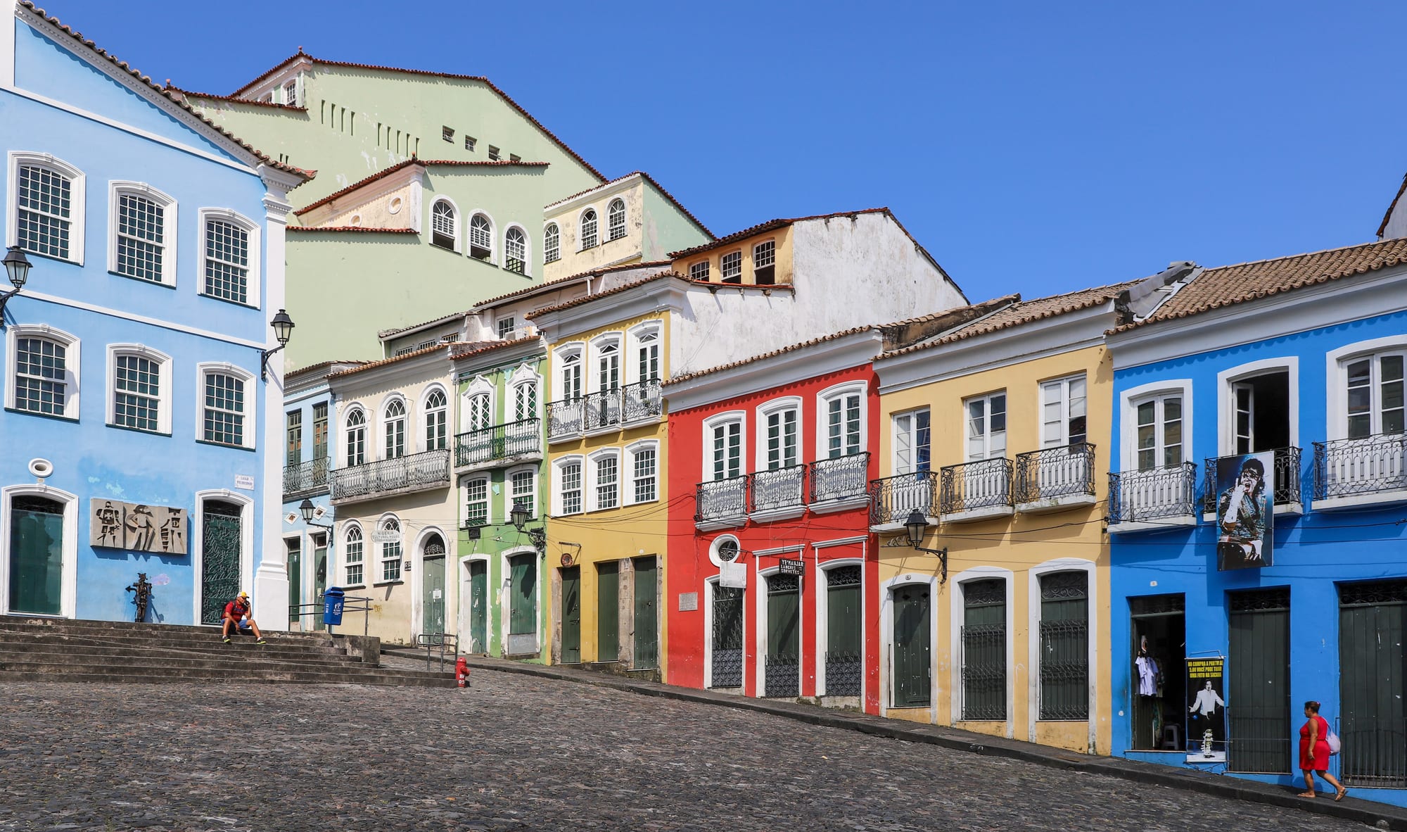 A steep cobbled square lined with brightly painted baroque colonial buildings and a blue church