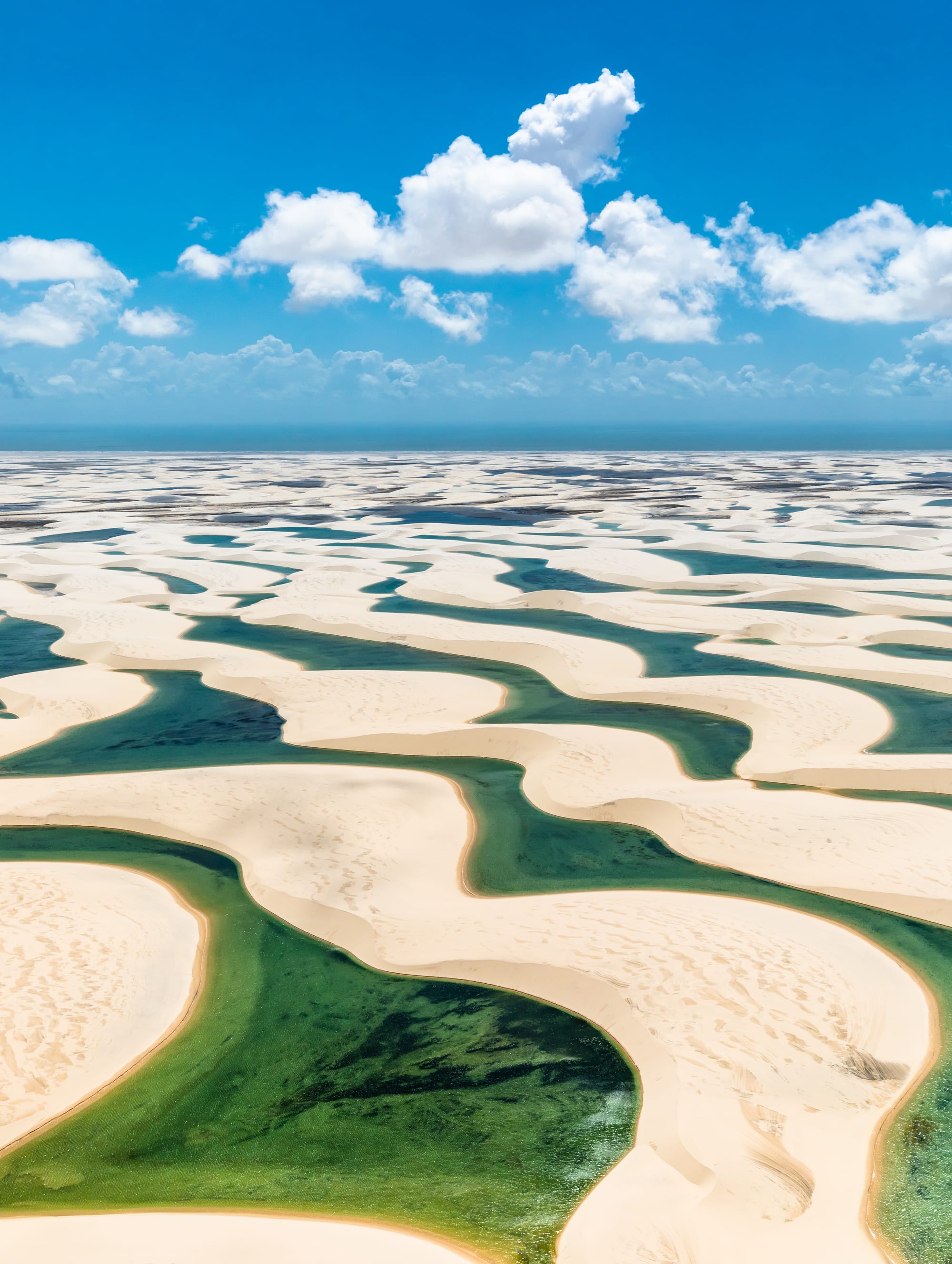 Rolling white sand dunes with pools of bright blue-green water in the hollows between them