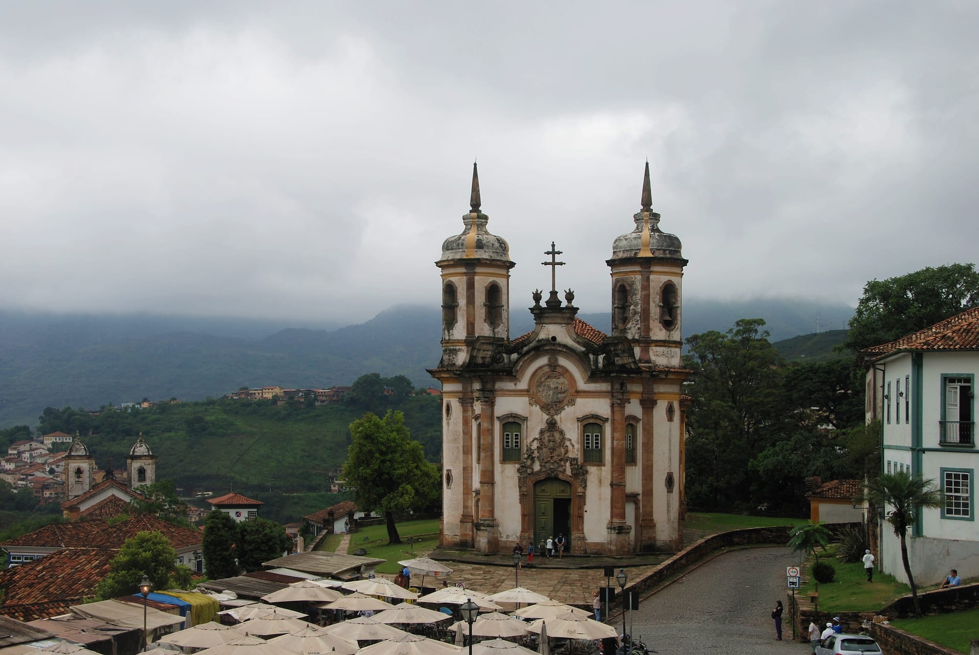 A hillside town of white colonial houses and baroque church towers under green mountains
