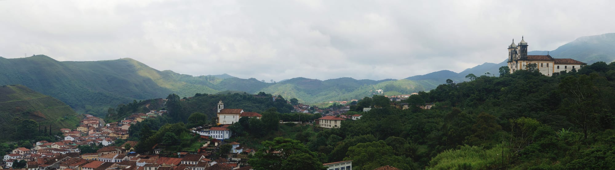 A hillside colonial town of white houses with red roofs and many baroque church towers, ringed by green mountains