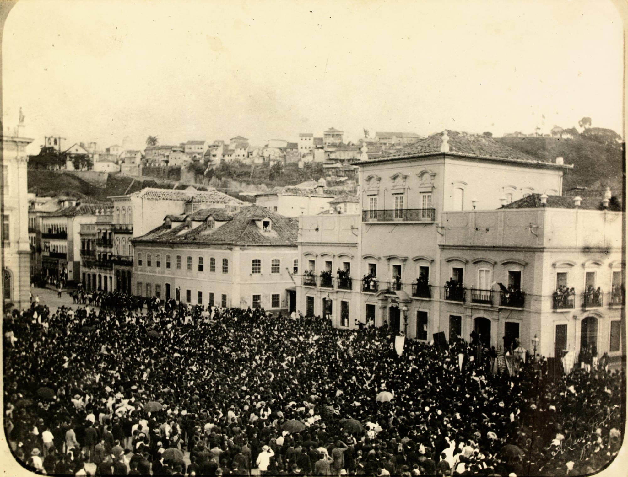 A large 1888 crowd of well-dressed people filling a Rio square, some waving hats, celebrating