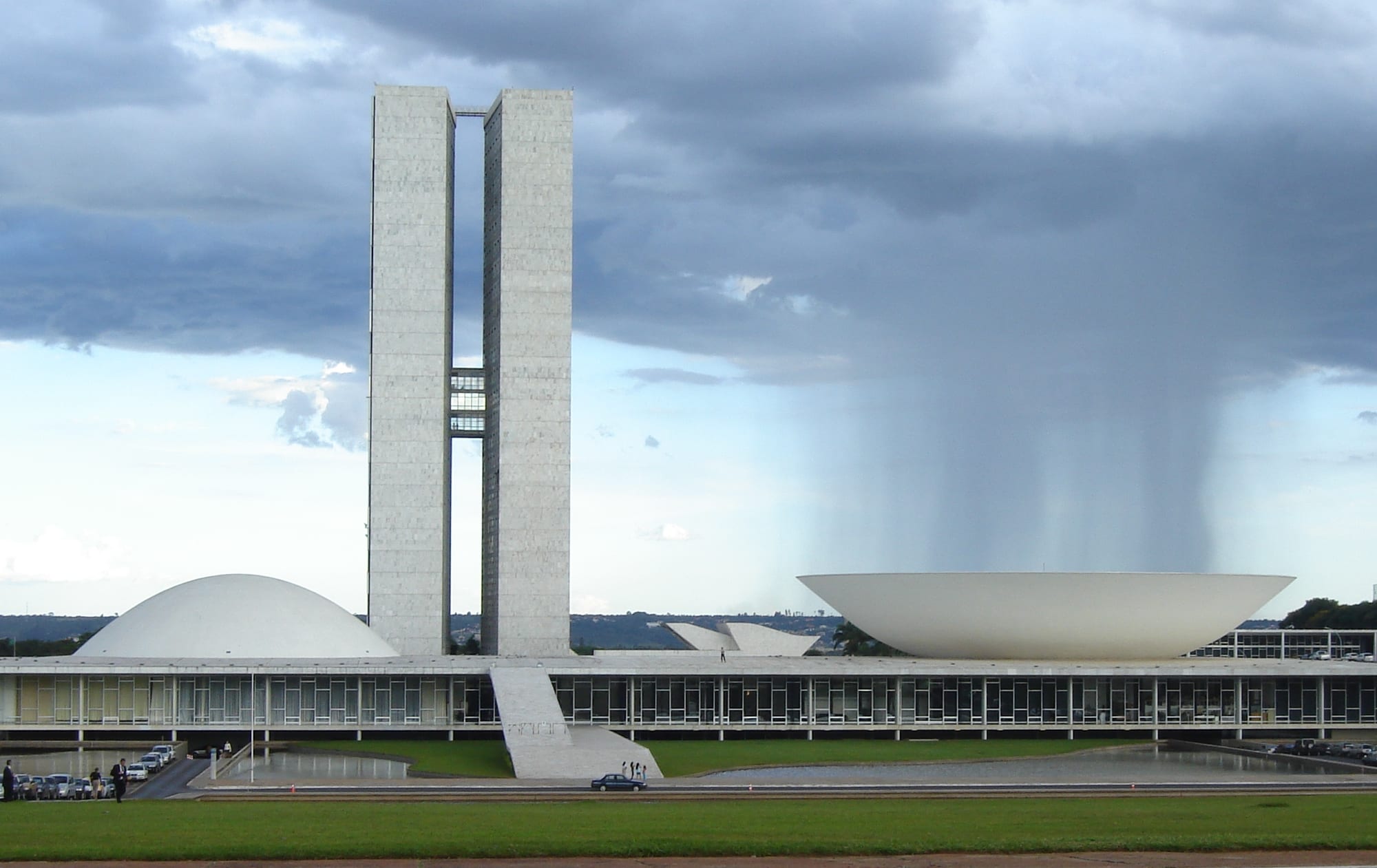 A low modernist government building with twin towers and two large white bowls, one domed, one upturned