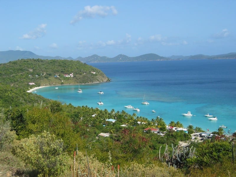 A curving white beach with a shallow turquoise lagoon behind a reef, a few low bars among the palms