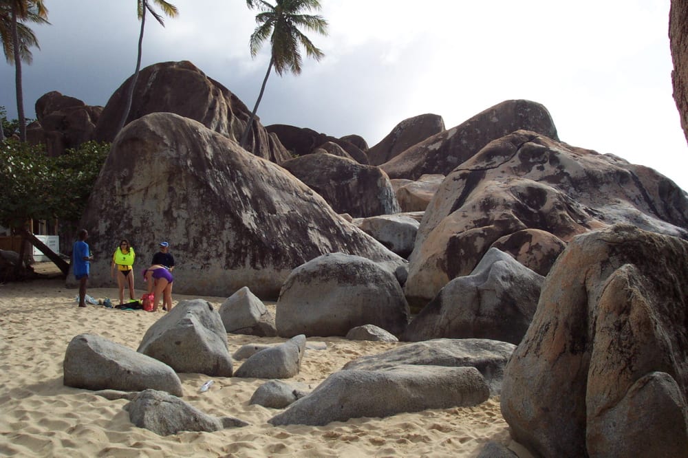 Enormous rounded granite boulders piled on a white beach forming shady caves and pools of clear water