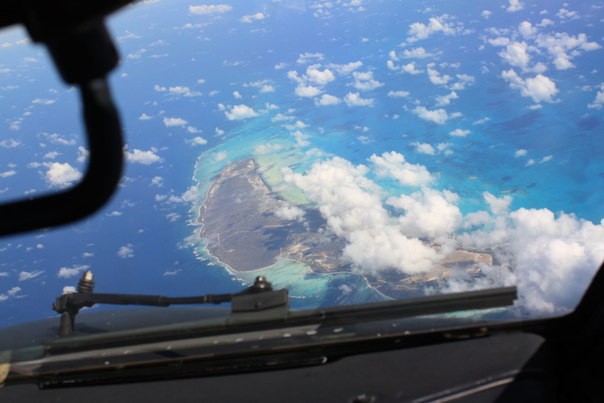 A completely flat sandy island with scrub, a vast pale reef flat and empty beach