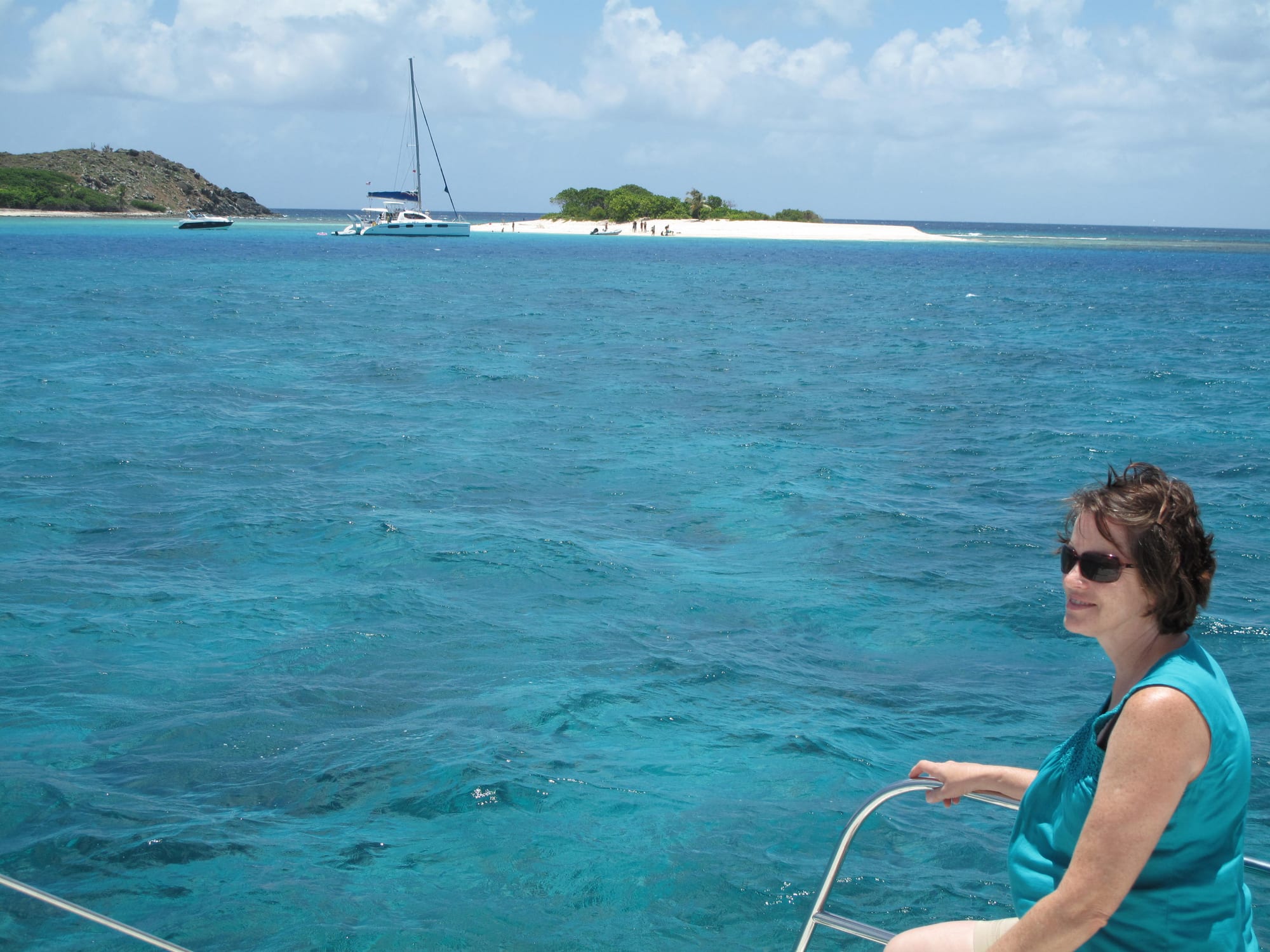 A tiny circular islet of white sand with a few palm trees, ringed by clear shallow water