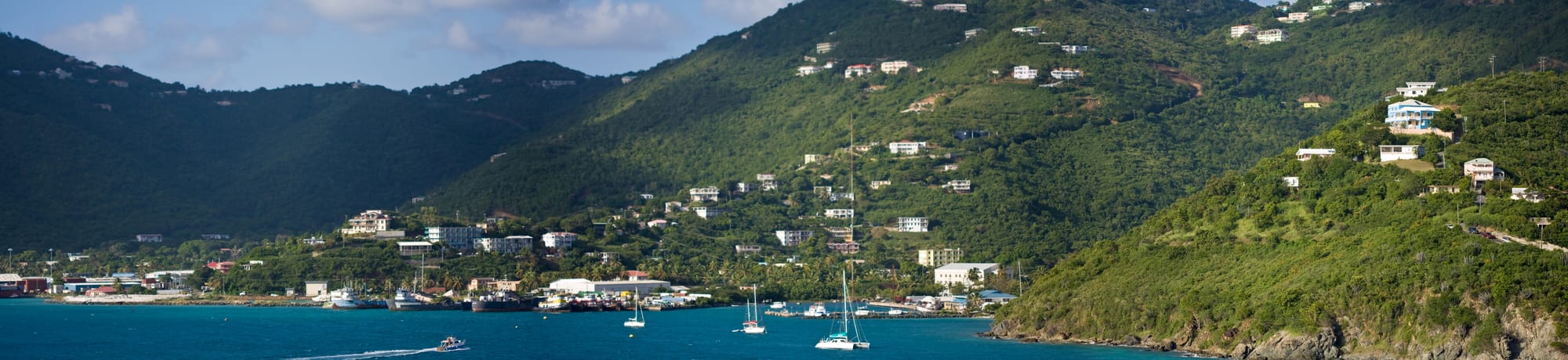 A small harbour town of low buildings around a bay full of yachts and a cruise dock
