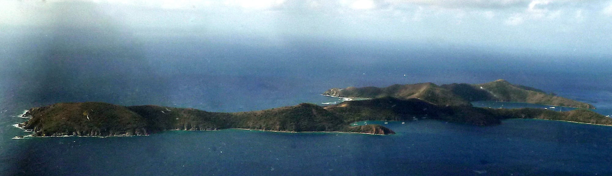 A green uninhabited island with a rocky coastline and clear surrounding water