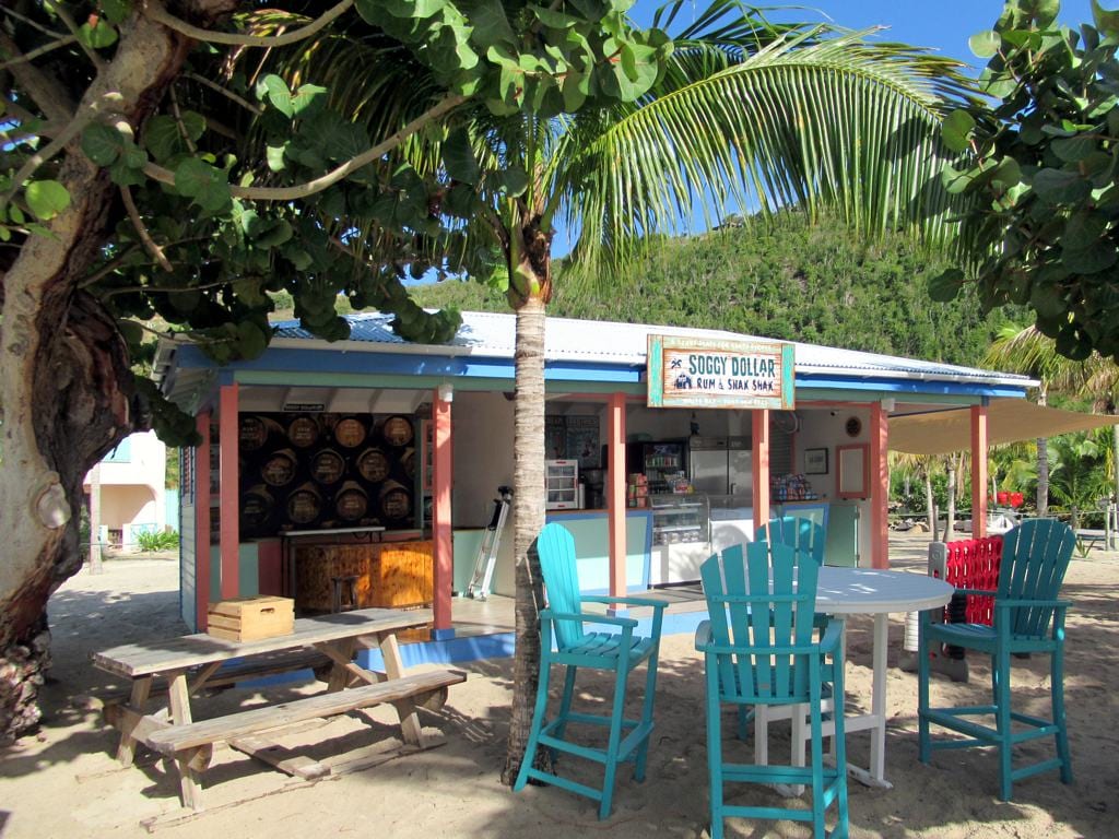 A beachfront bar with a thatched roof and outdoor seating on a sandy beach