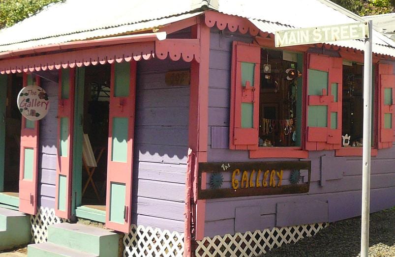 A colourful purple and pink wooden shop building on Main Street with open shutter windows displaying goods for sale