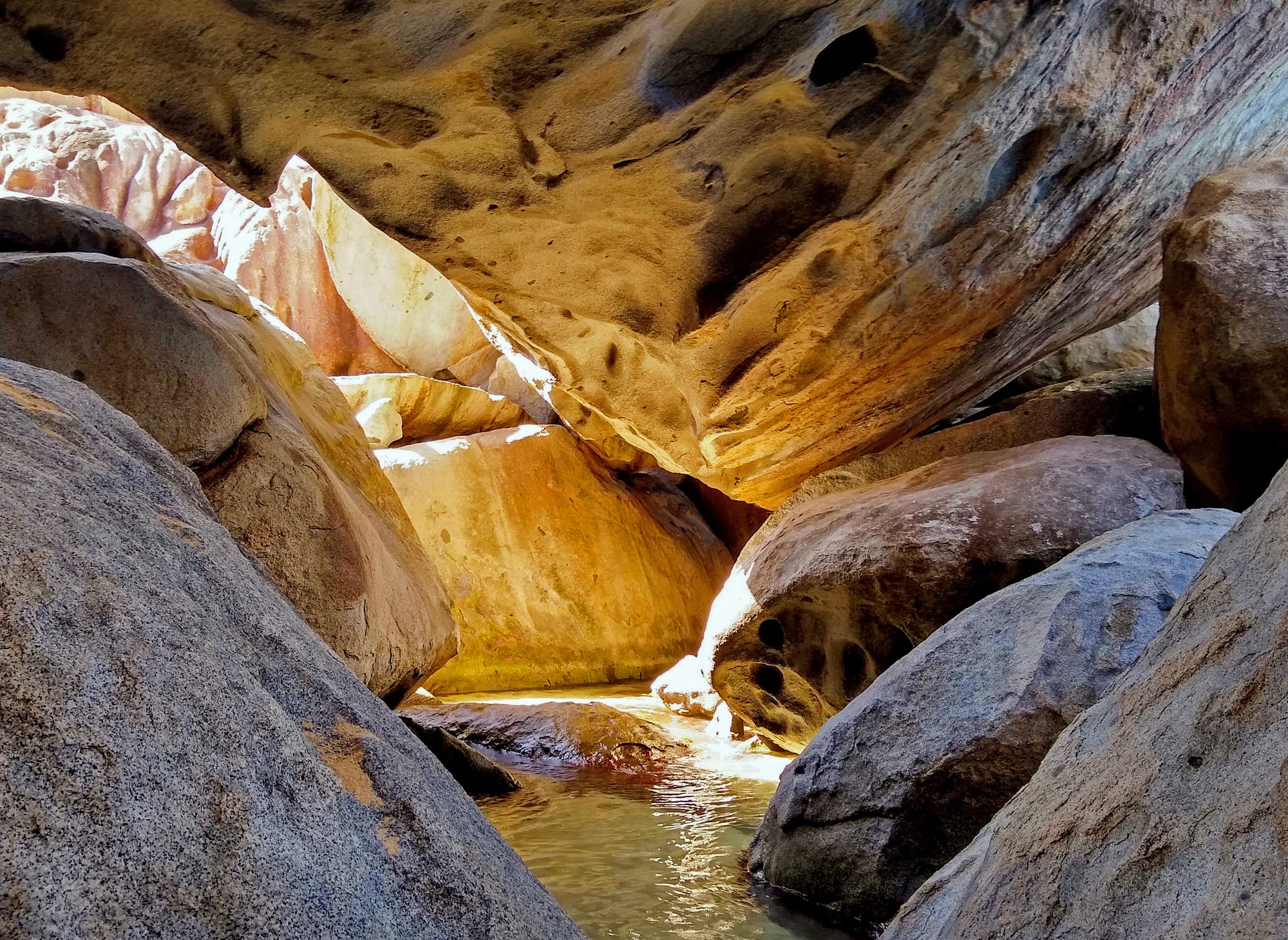 Huge rounded granite boulders forming grottoes and pools along a white-sand beach with clear water