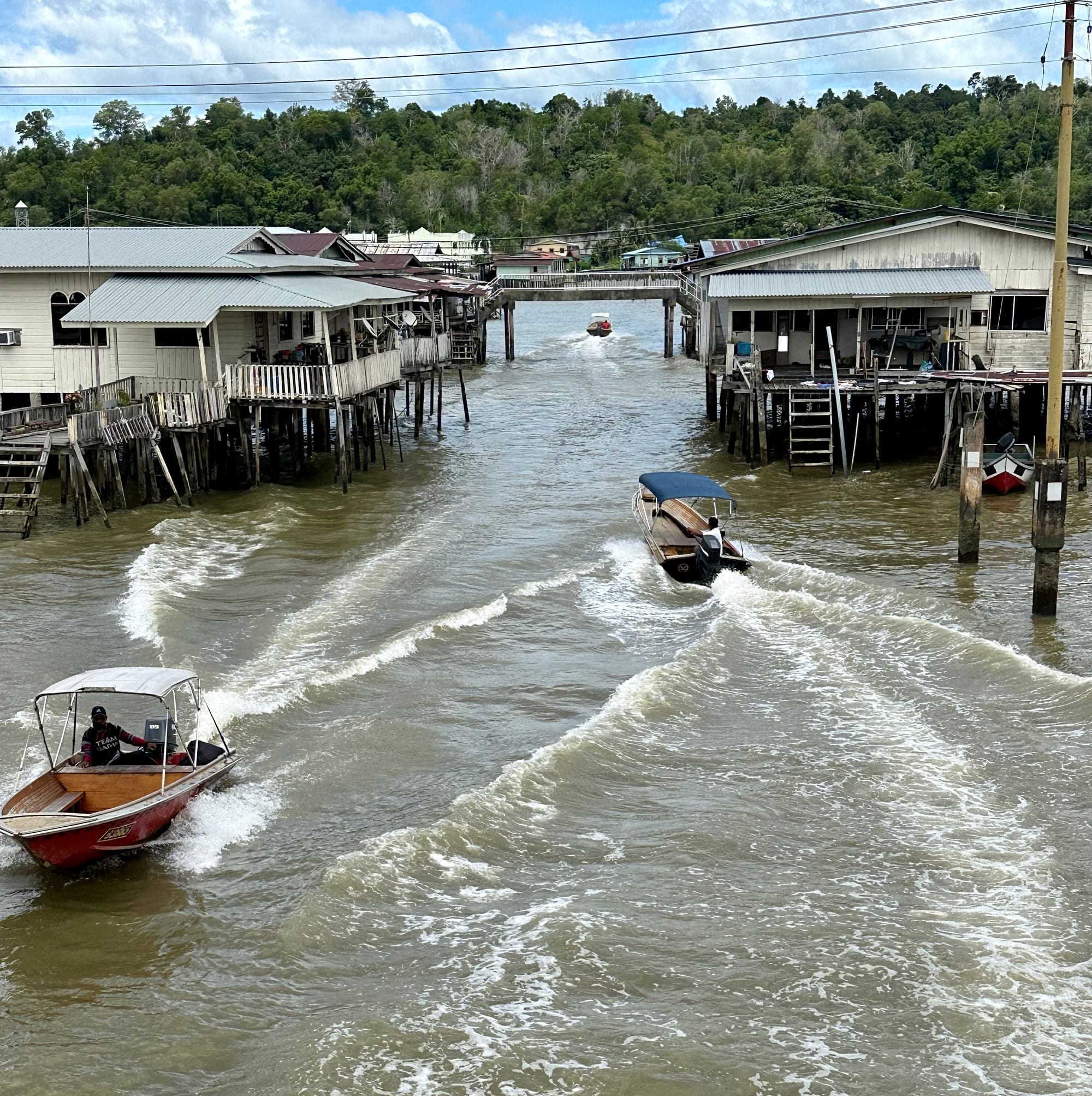 Small motor boats speeding along a water channel lined with wooden stilt houses in Kampong Ayer, Brunei