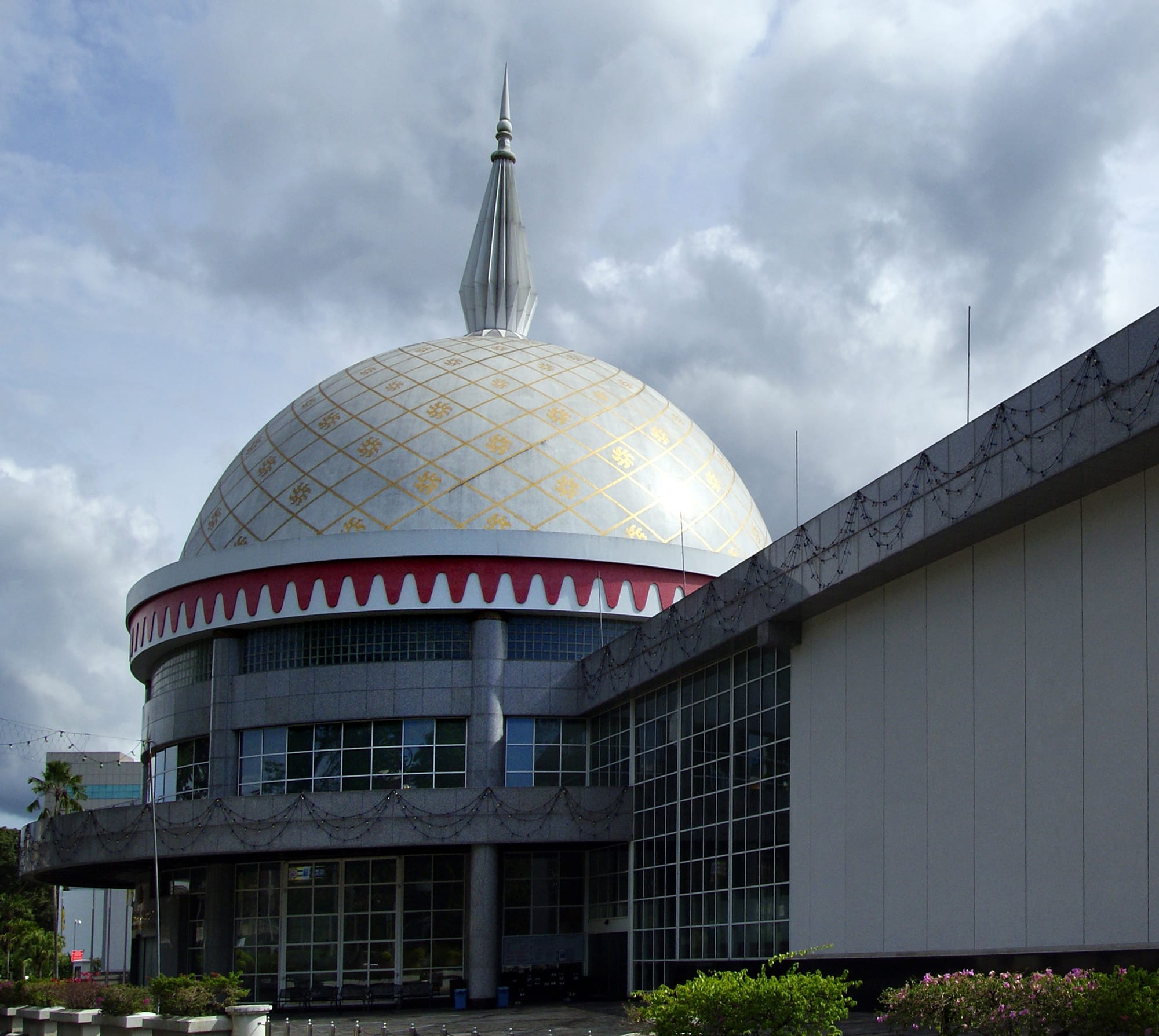 A domed white ceremonial building with a wide plaza and flagpoles in front