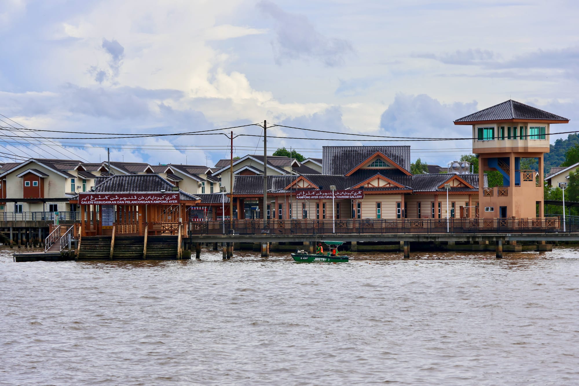A tidy waterfront promenade with the water village and a mosque dome across the river