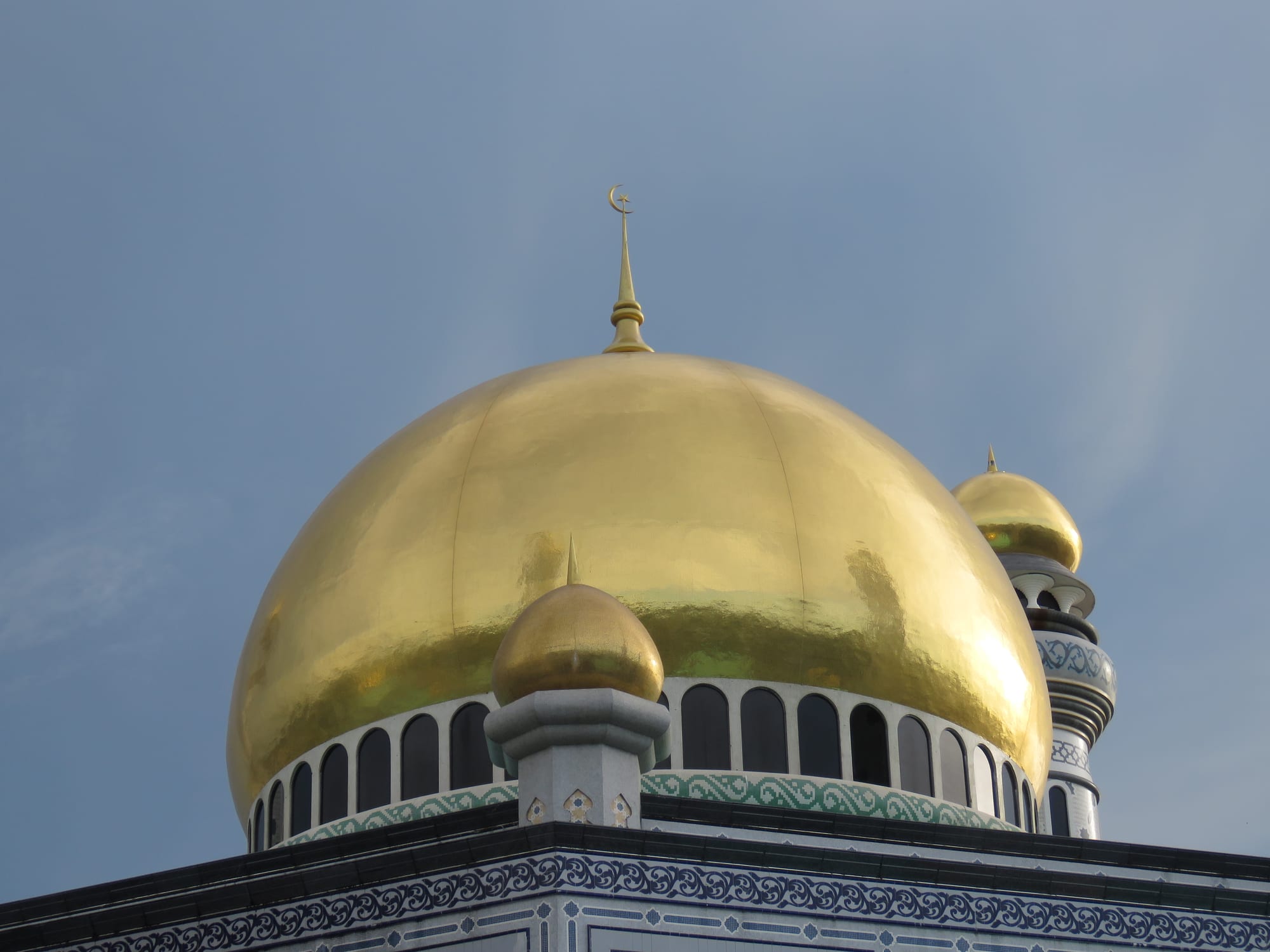 An enormous mosque with four minarets and multiple blue-and-gold domes set in formal gardens
