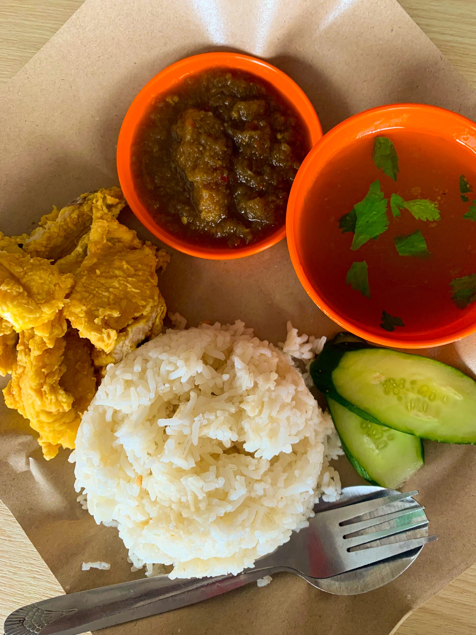A plate of white rice topped with fried chicken and a spoonful of chilli sambal