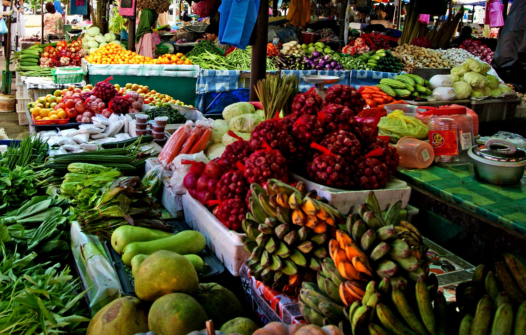 A busy open-air market with food stalls and produce displayed under a covered roof