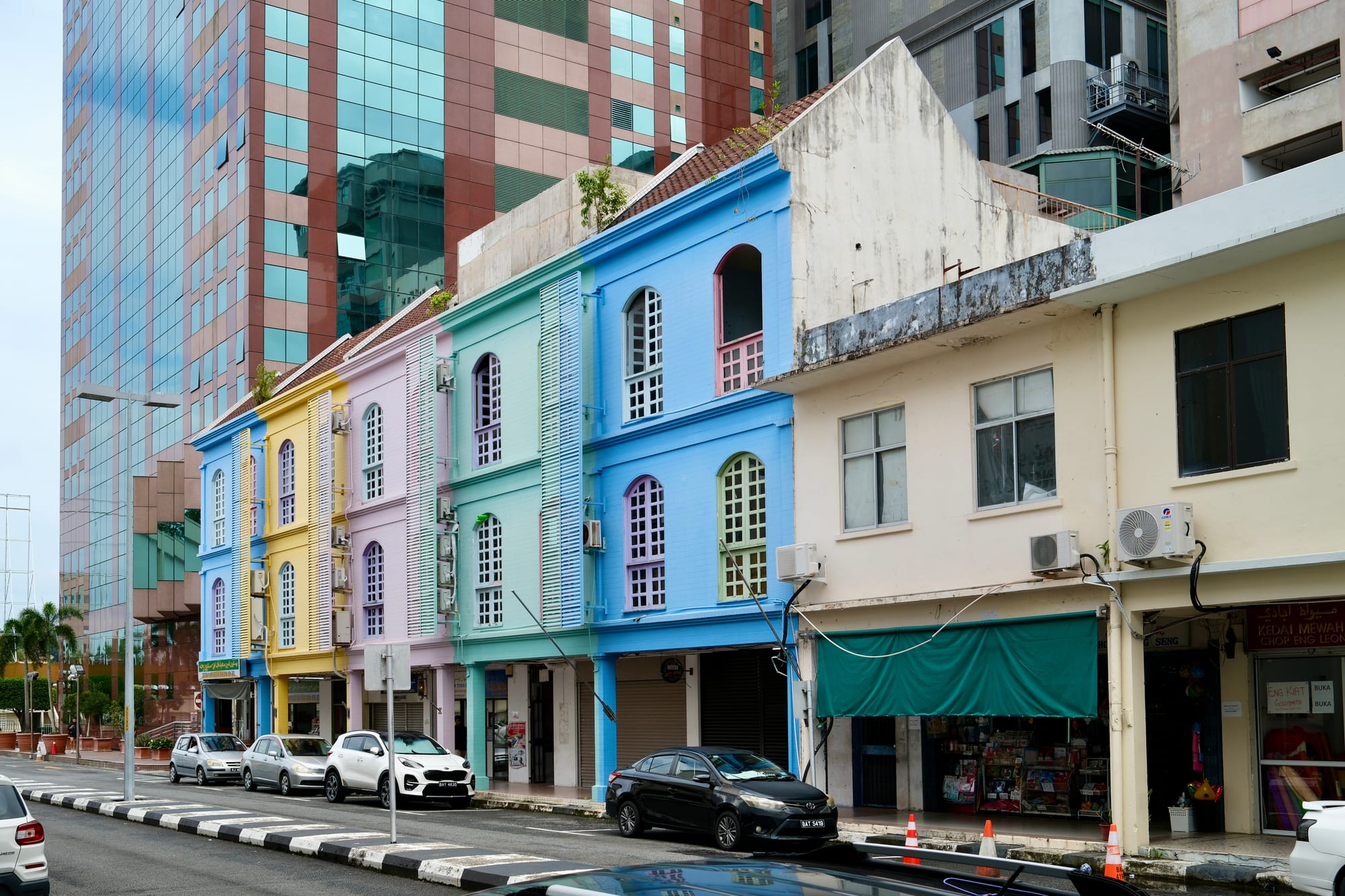 A row of two-storey colonial shophouses with arched arcades on a quiet street in a tropical town