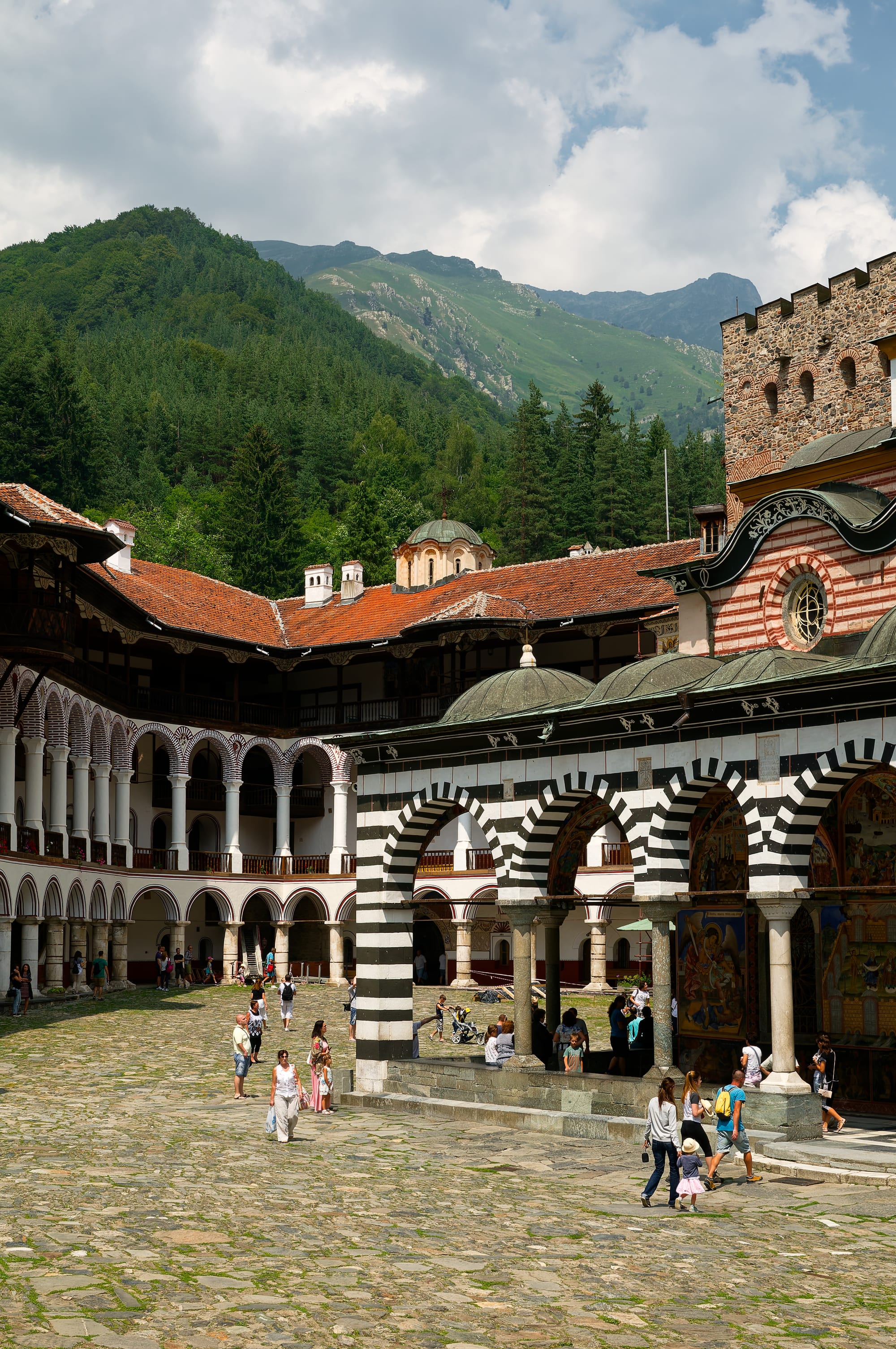 A monastery courtyard ringed by black-and-white striped arcaded galleries around a domed painted church