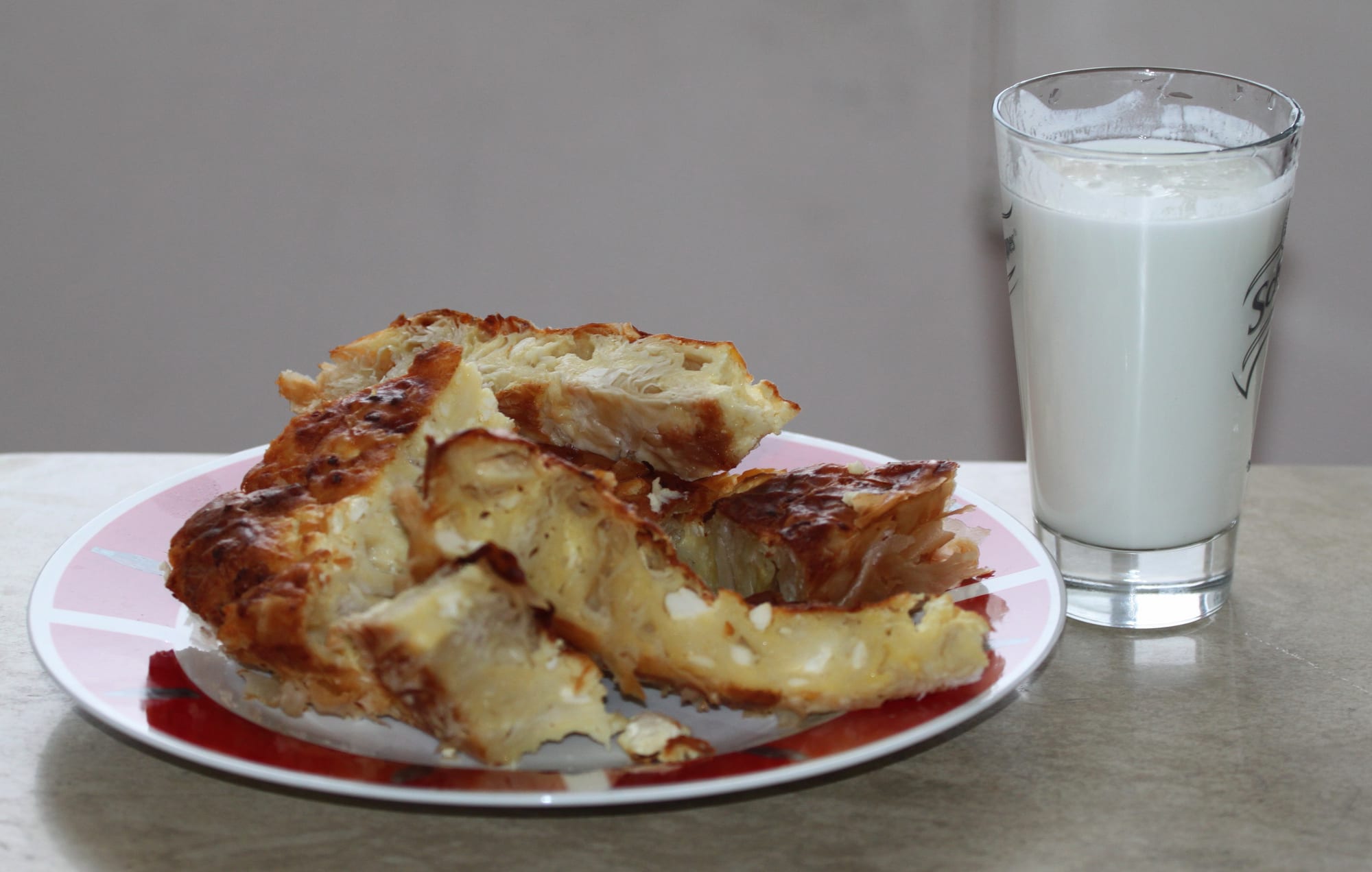 A golden, coiled filo pastry pie beside a glass of yogurt drink