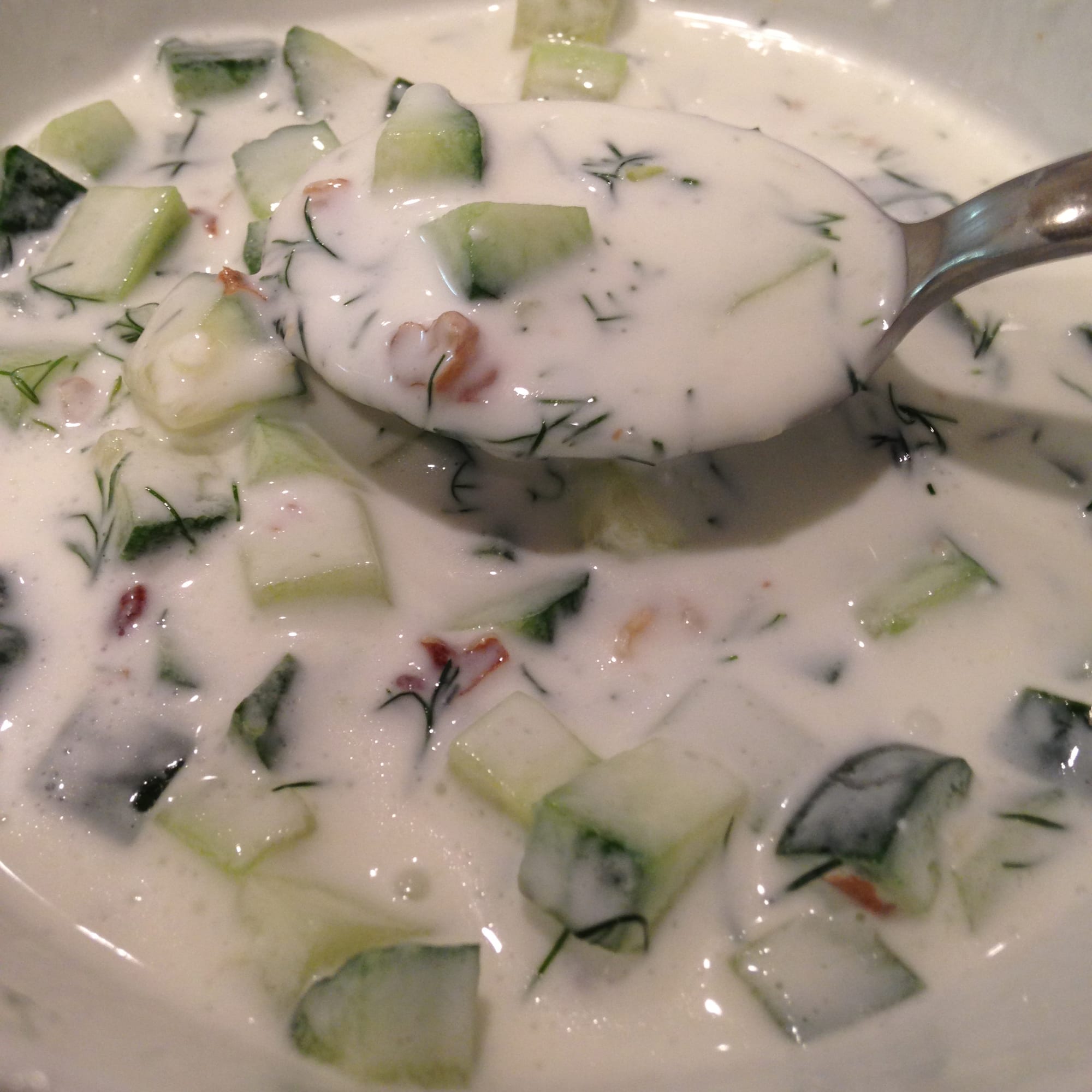 A bowl of pale, thick soup with diced cucumber and chopped walnuts on top