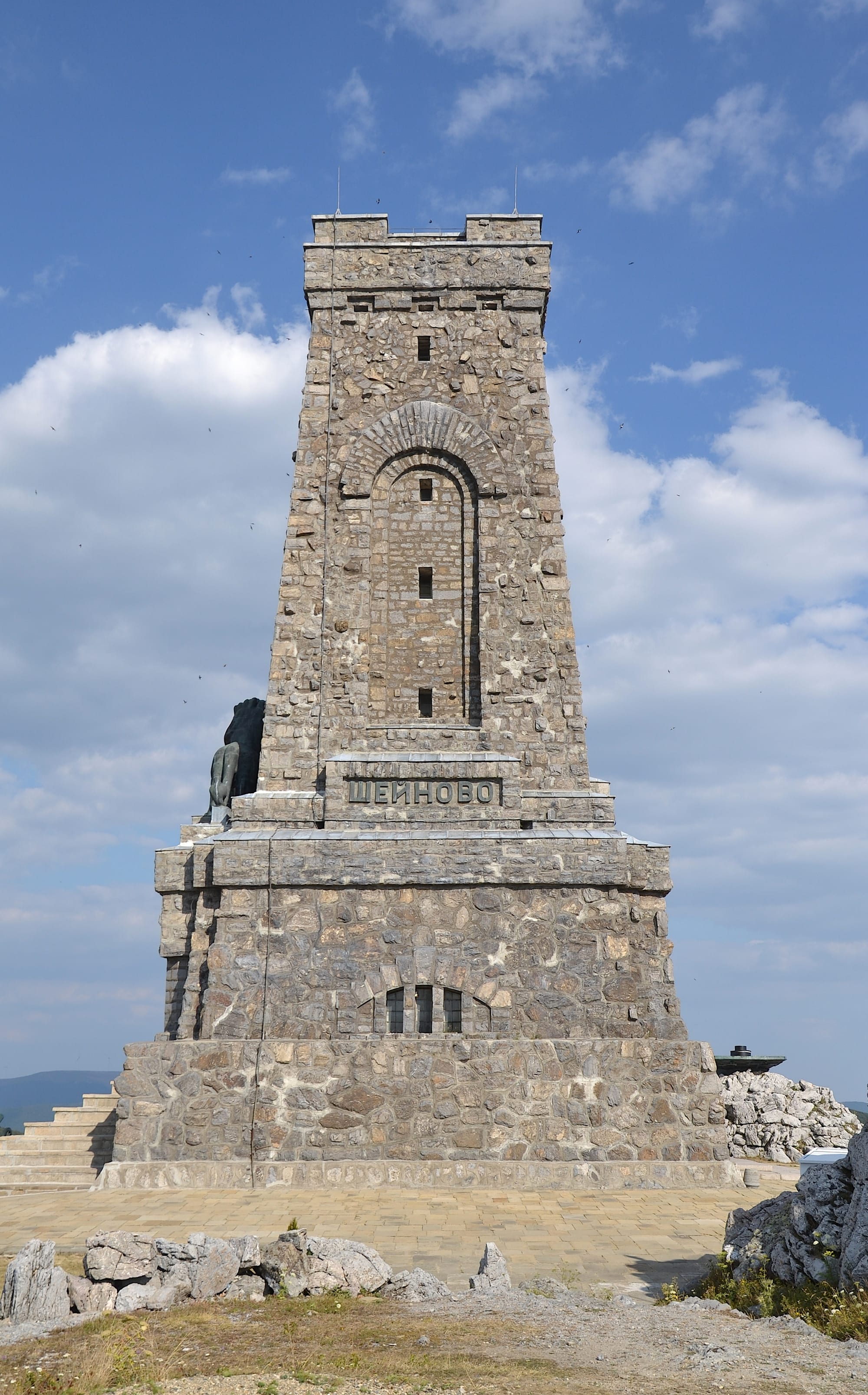 A tall stone tower monument on a bare mountain ridge, with a bronze lion above the door