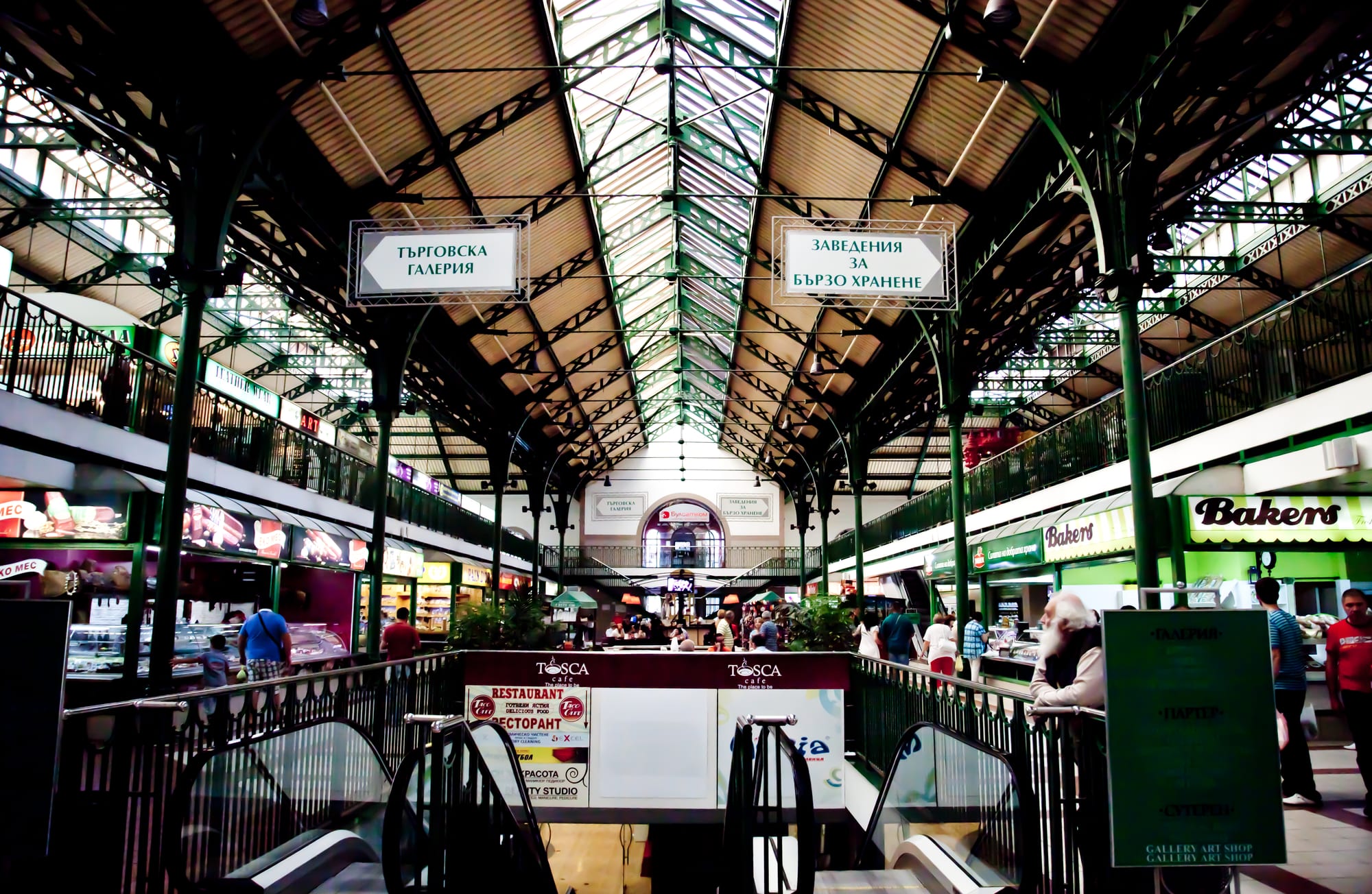 The vaulted glass-roofed interior of Sofia's Central Market Hall, lined with food stalls and shoppers