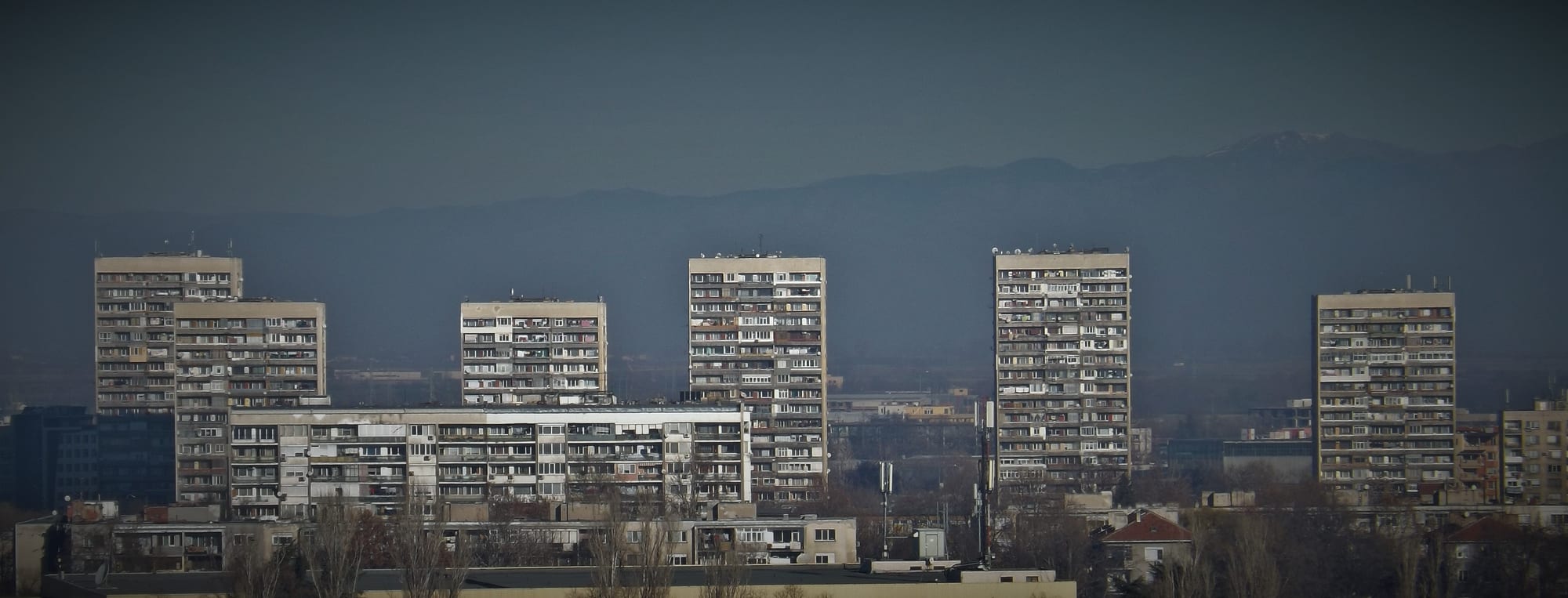 A row of tall concrete panel apartment blocks against a mountain skyline near Plovdiv