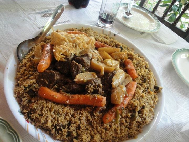 A plate of reddish, oil-glossed rice with a piece of meat on top