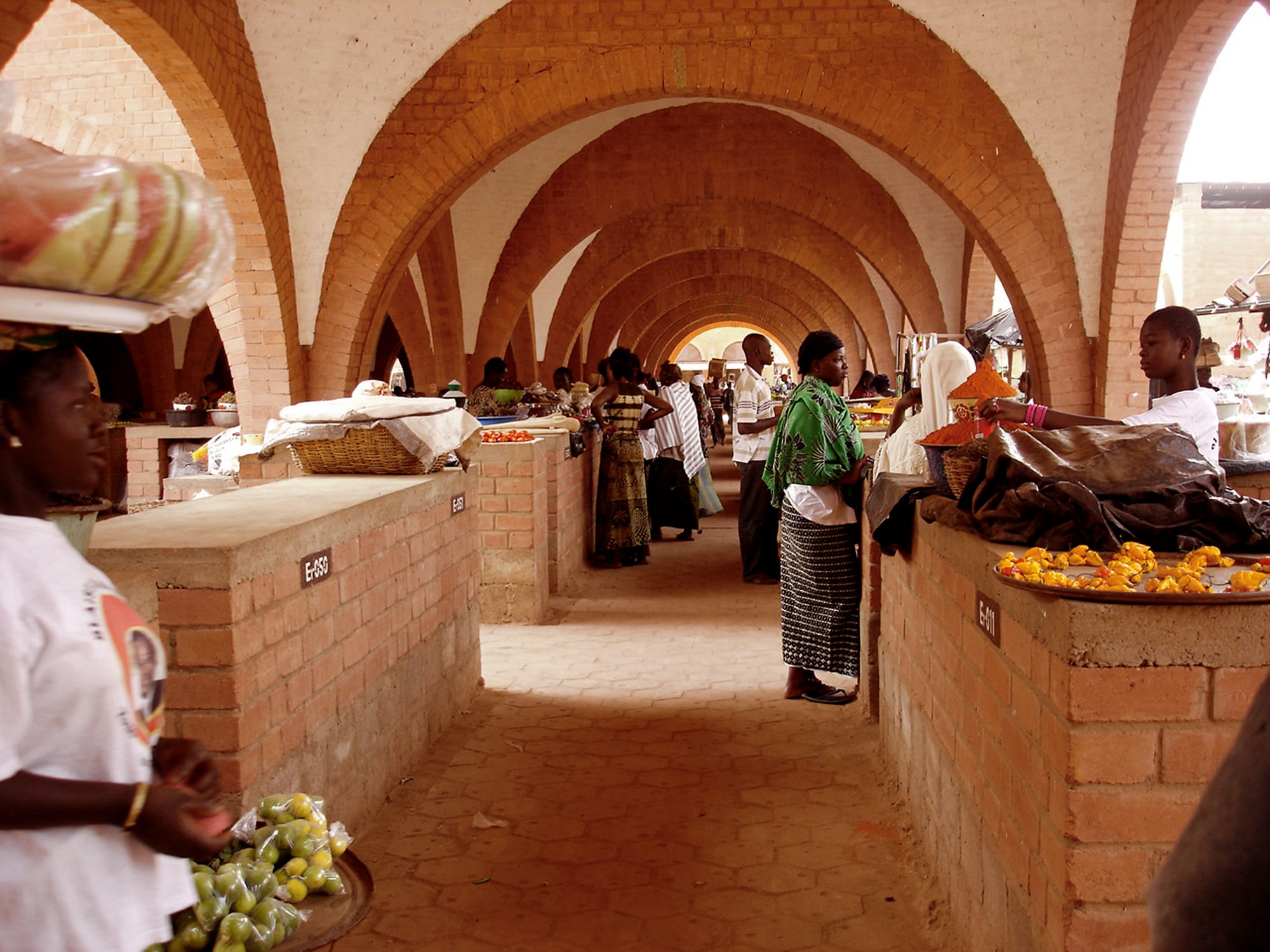 A vaulted brick market hall in Burkina Faso, its arched corridors lined with stalls and shoppers