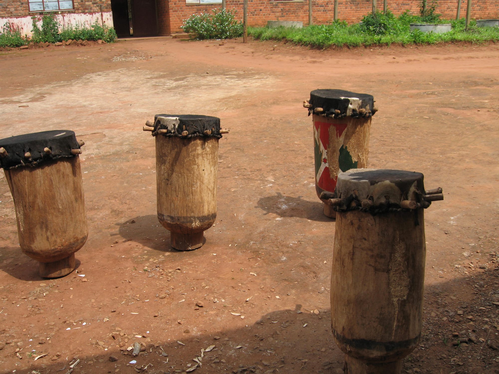A line of men in white, red and green robes balancing tall wooden drums on their heads, mid-dance