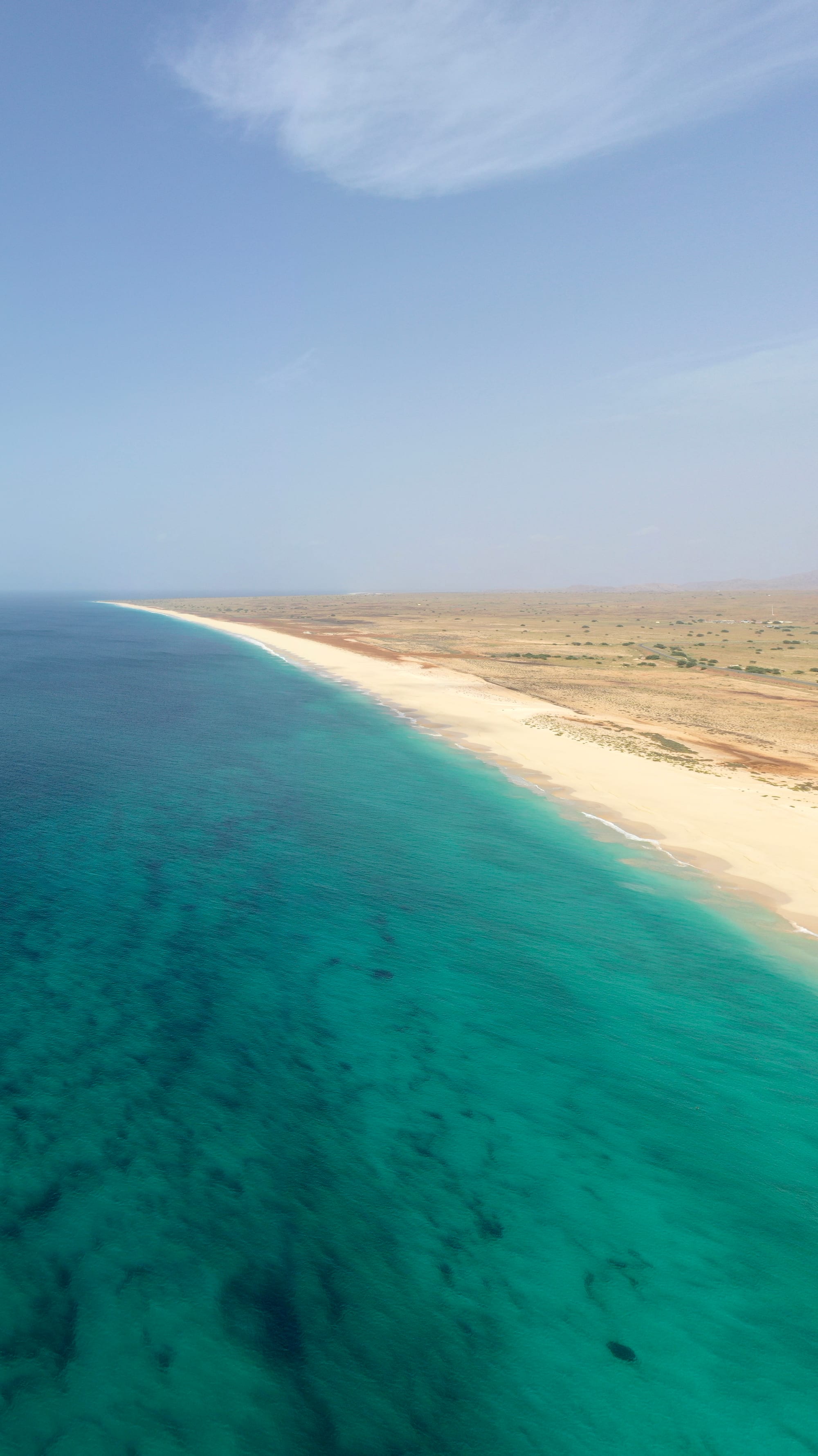 An empty golden beach curving away under a pale sky, with turquoise water alongside