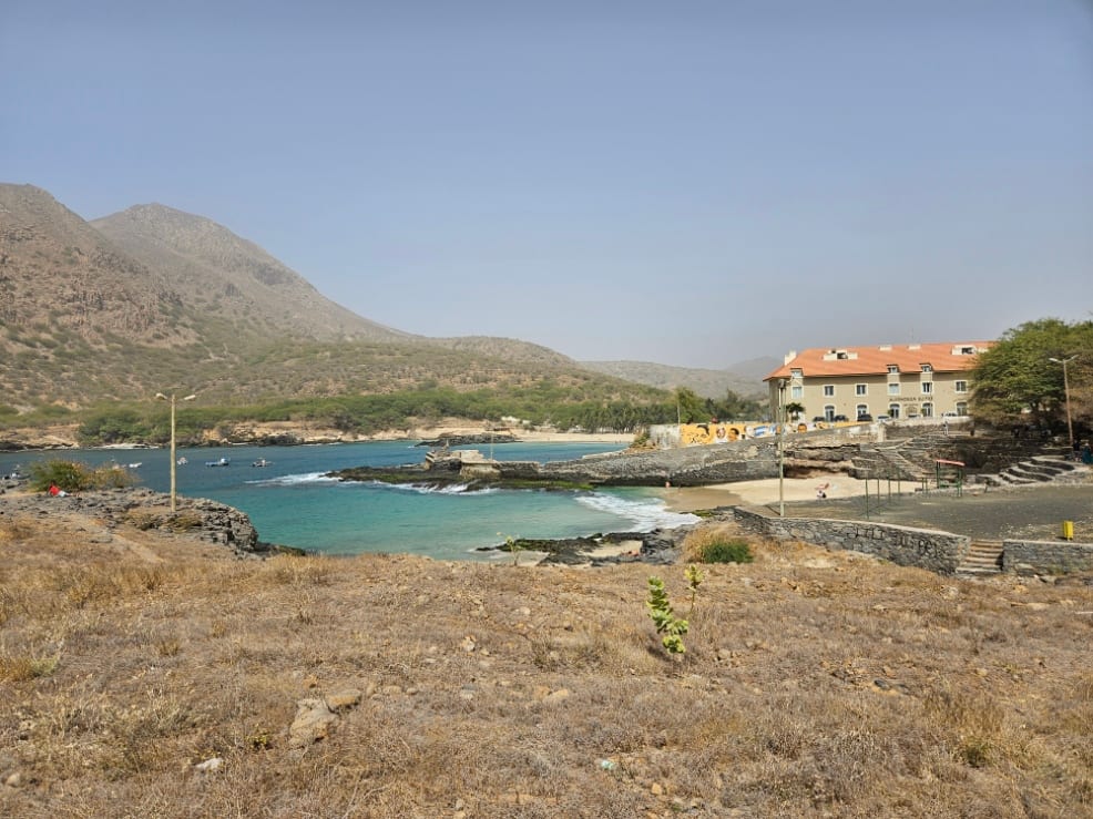 A calm bay of pale sand and blue water backed by dry hills