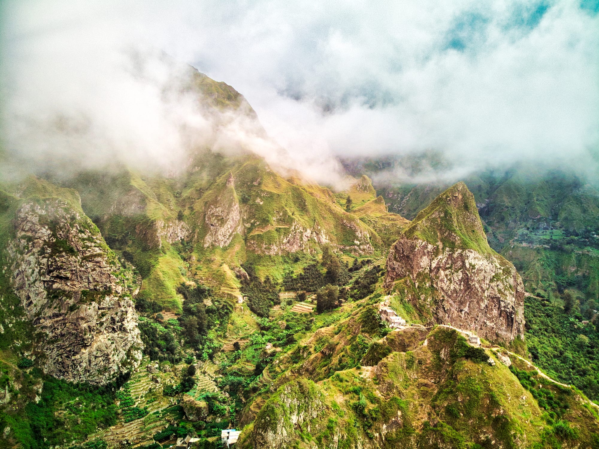A deep green valley of terraced fields and palms winding between sharp volcanic ridges down to the sea