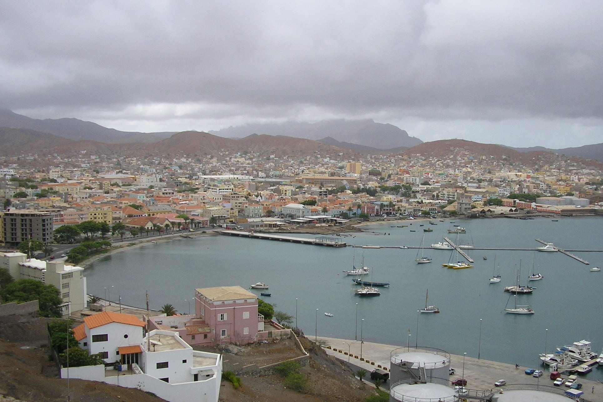 A colourful port town around a bay, with pastel colonial buildings and hills behind