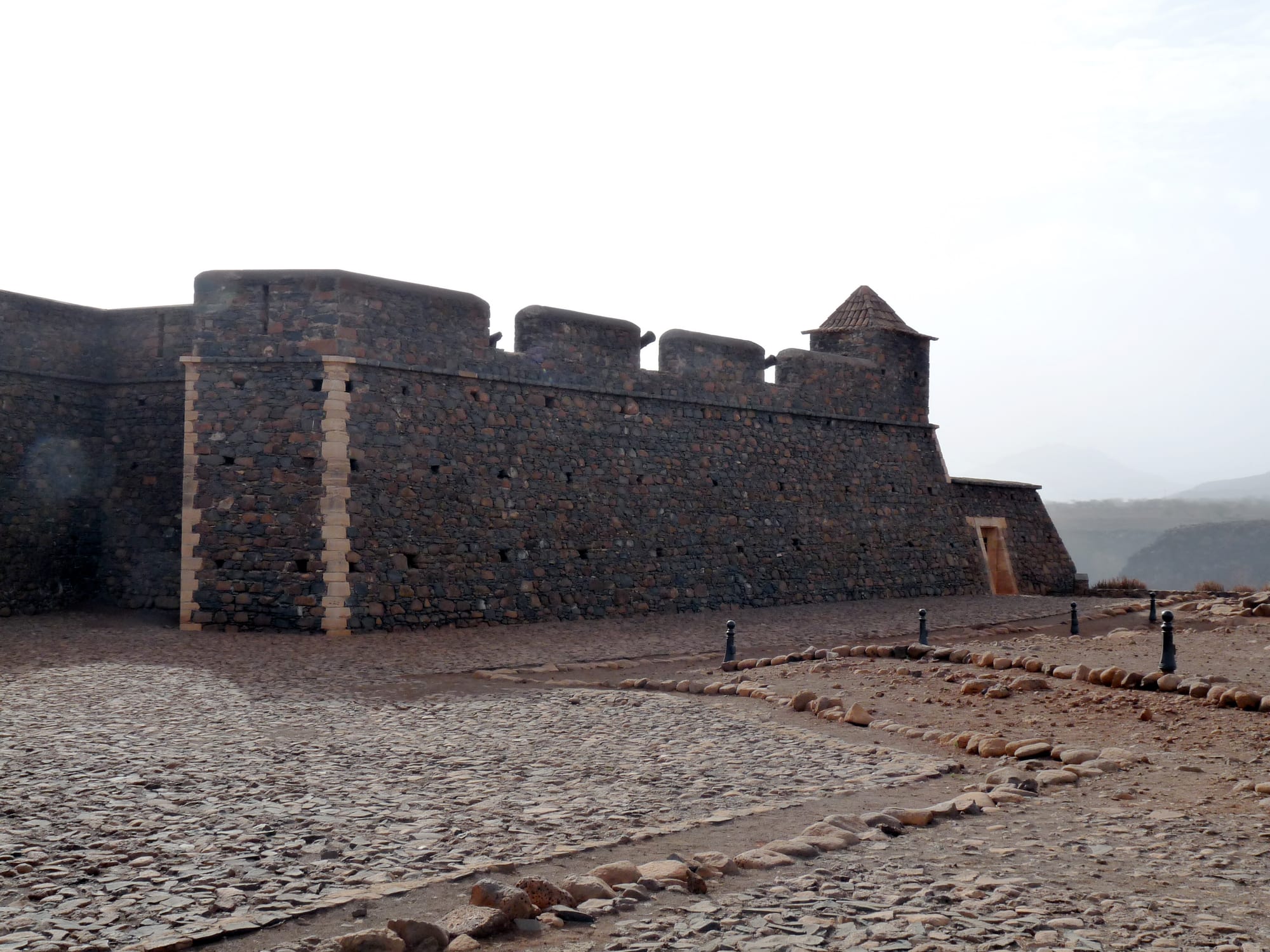 A star-shaped stone fort with cannon on a bare hilltop above a small town and a blue bay